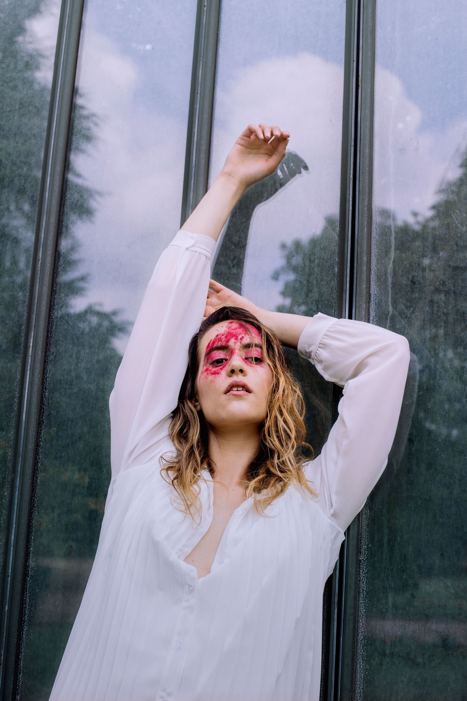 Woman in white shirt with red face paint posing by glass windows.