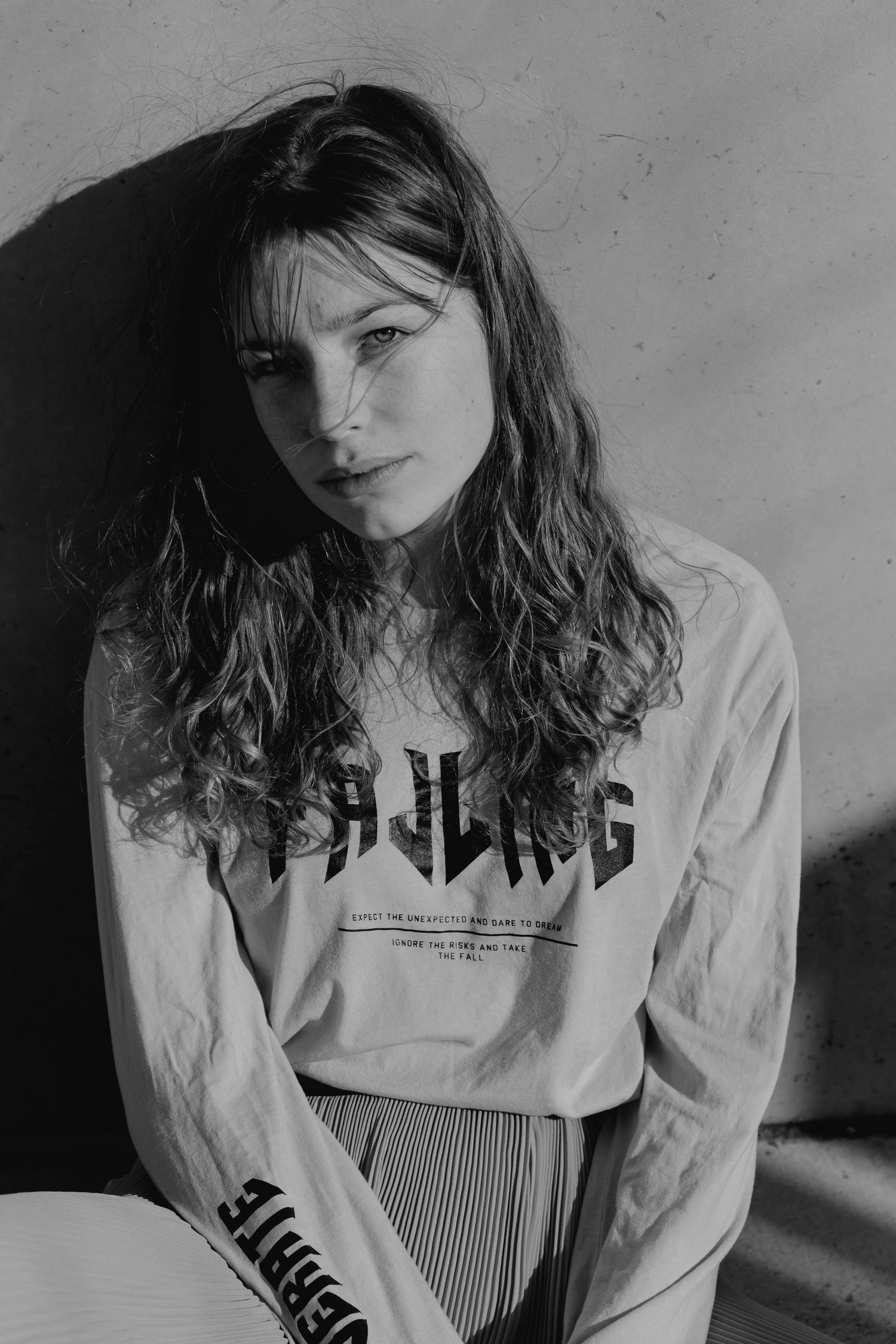 Black and white portrait of young woman in graphic long-sleeve shirt sitting in moody lighting.