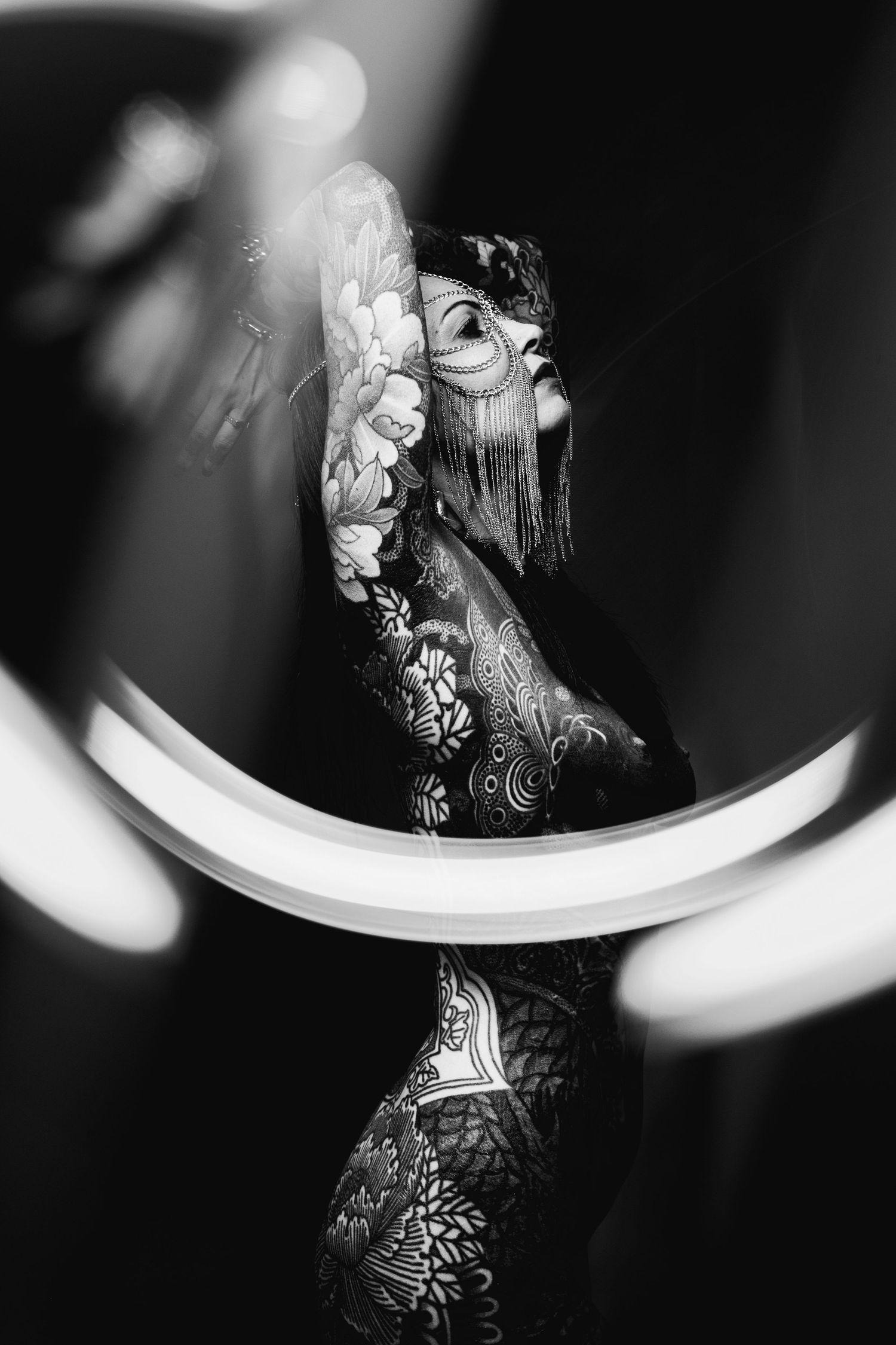 Black and white artistic photo of heavily tattooed woman posing with circular light ring reflection.