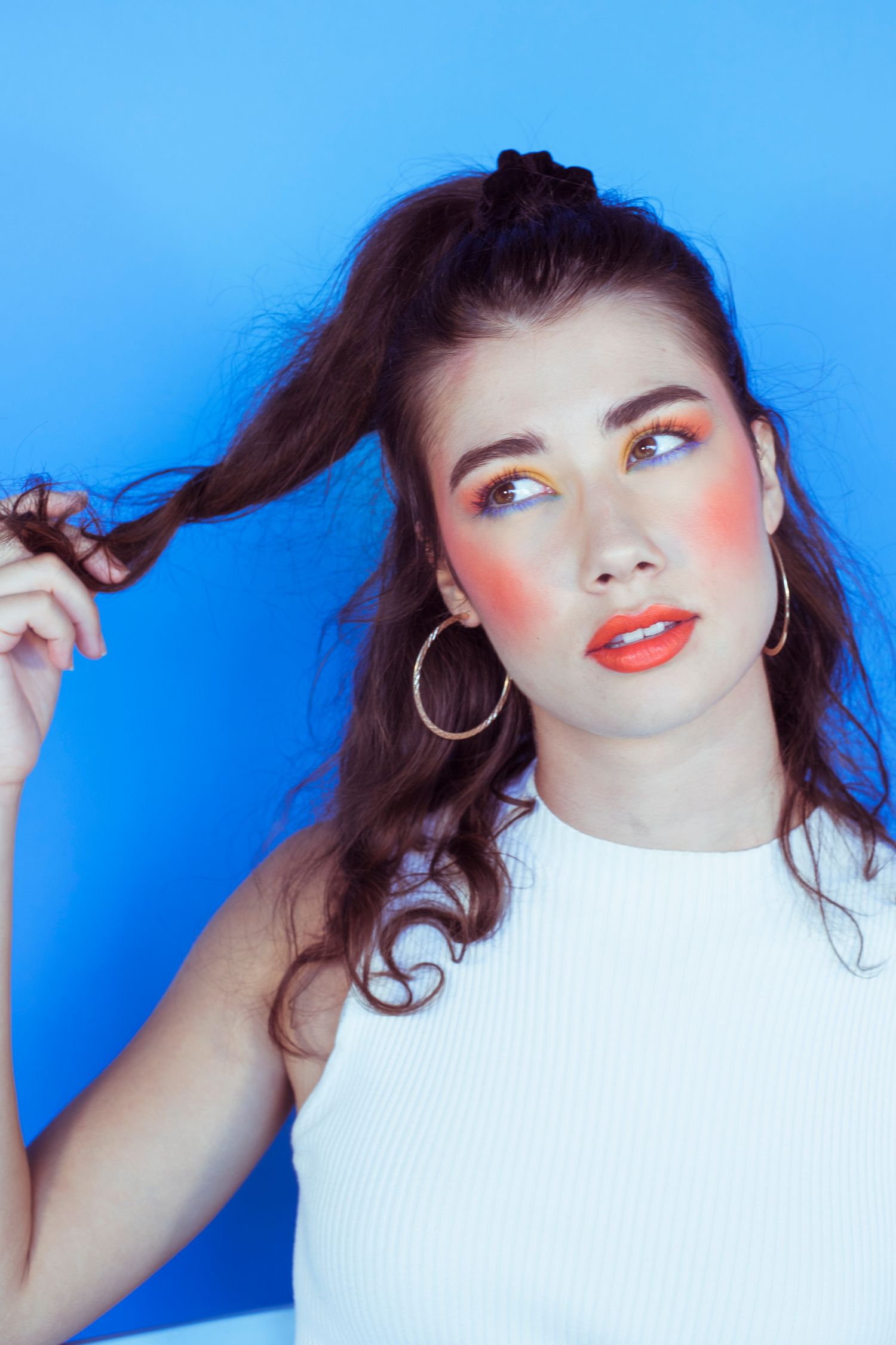 Brunette woman with colorful orange blush makeup on a blue background.