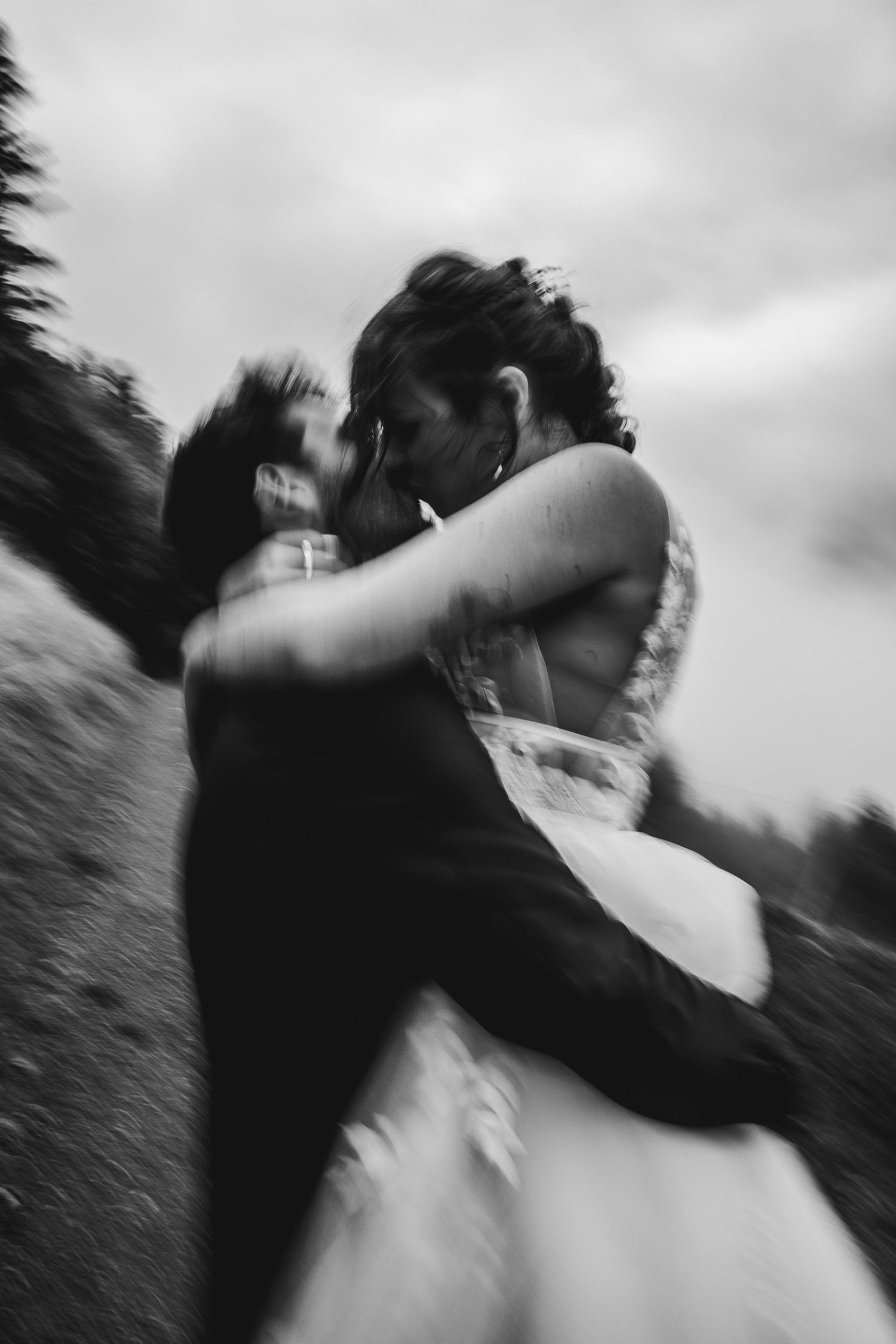Blurred artistic black and white photo of newlyweds kissing outdoors in nature.