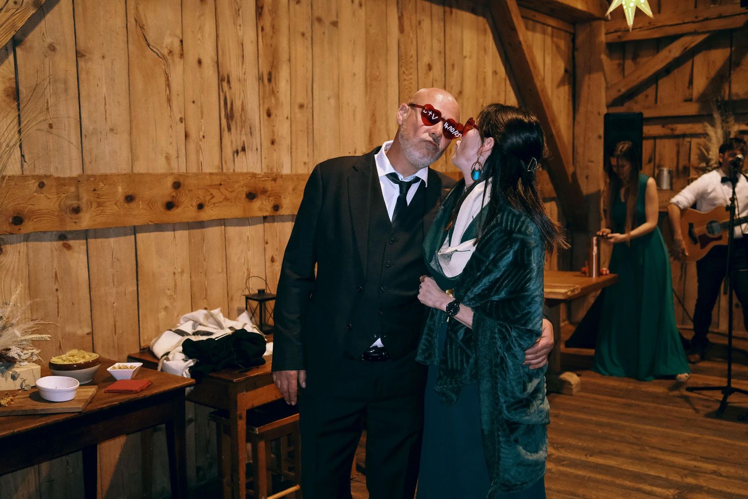 Couple shares a kiss wearing novelty red glasses at rustic barn wedding reception.