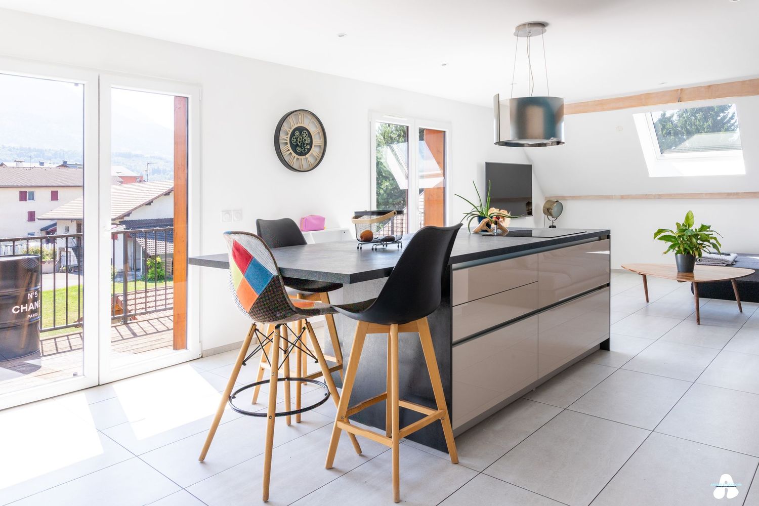 Modern open-plan kitchen with island, colorful bar stools and large windows overlooking balcony.