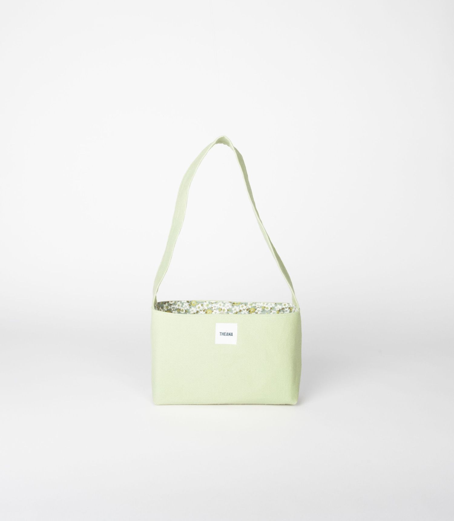 Light green small crossbody bag with floral interior lining and white label on a neutral background.