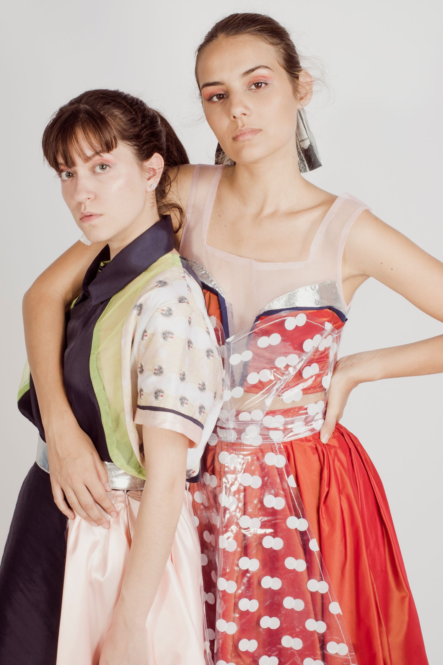Two female models posing together wearing colorful designer dresses on white background.