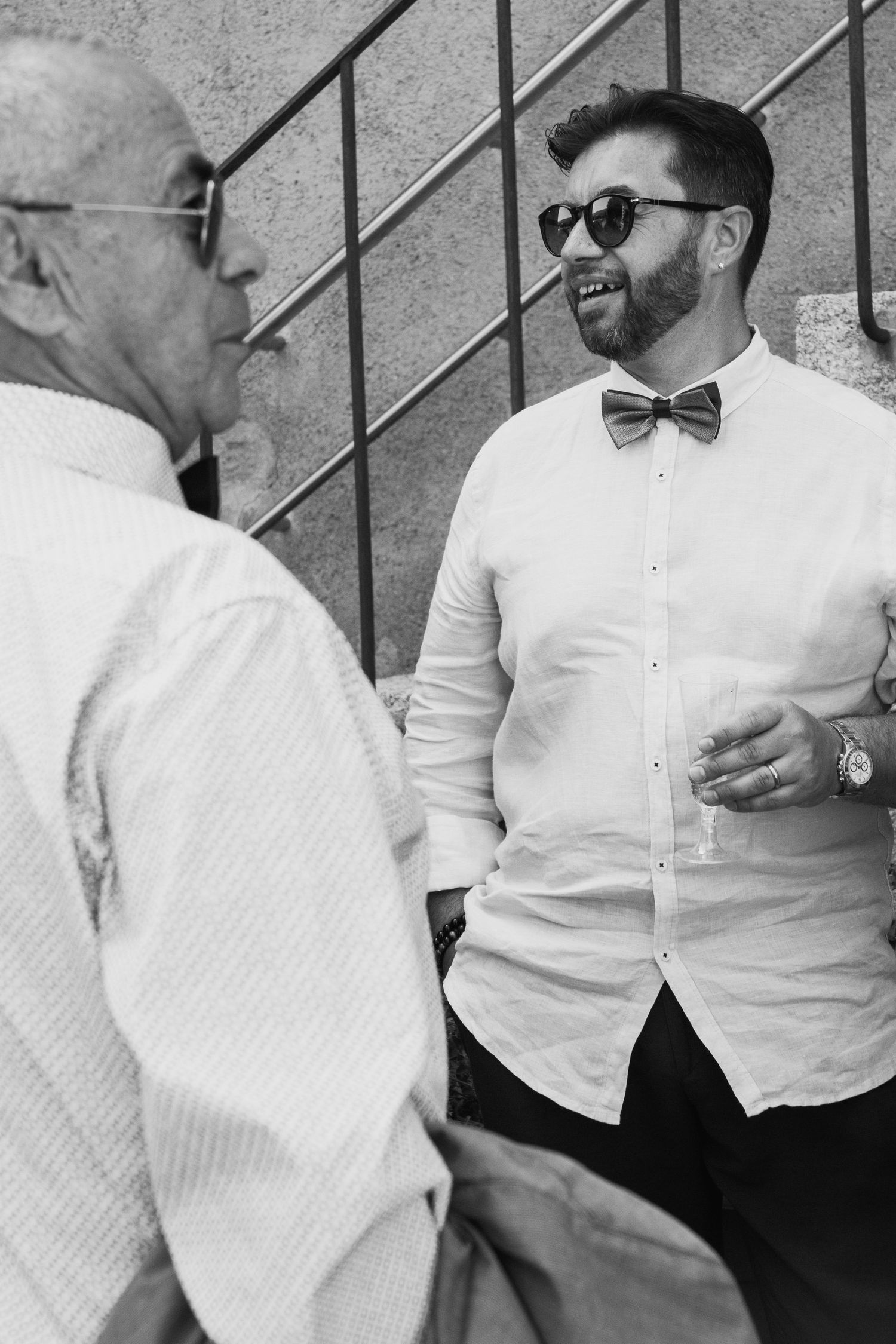 Black and white photo of two men in elegant attire laughing together at a wedding event.