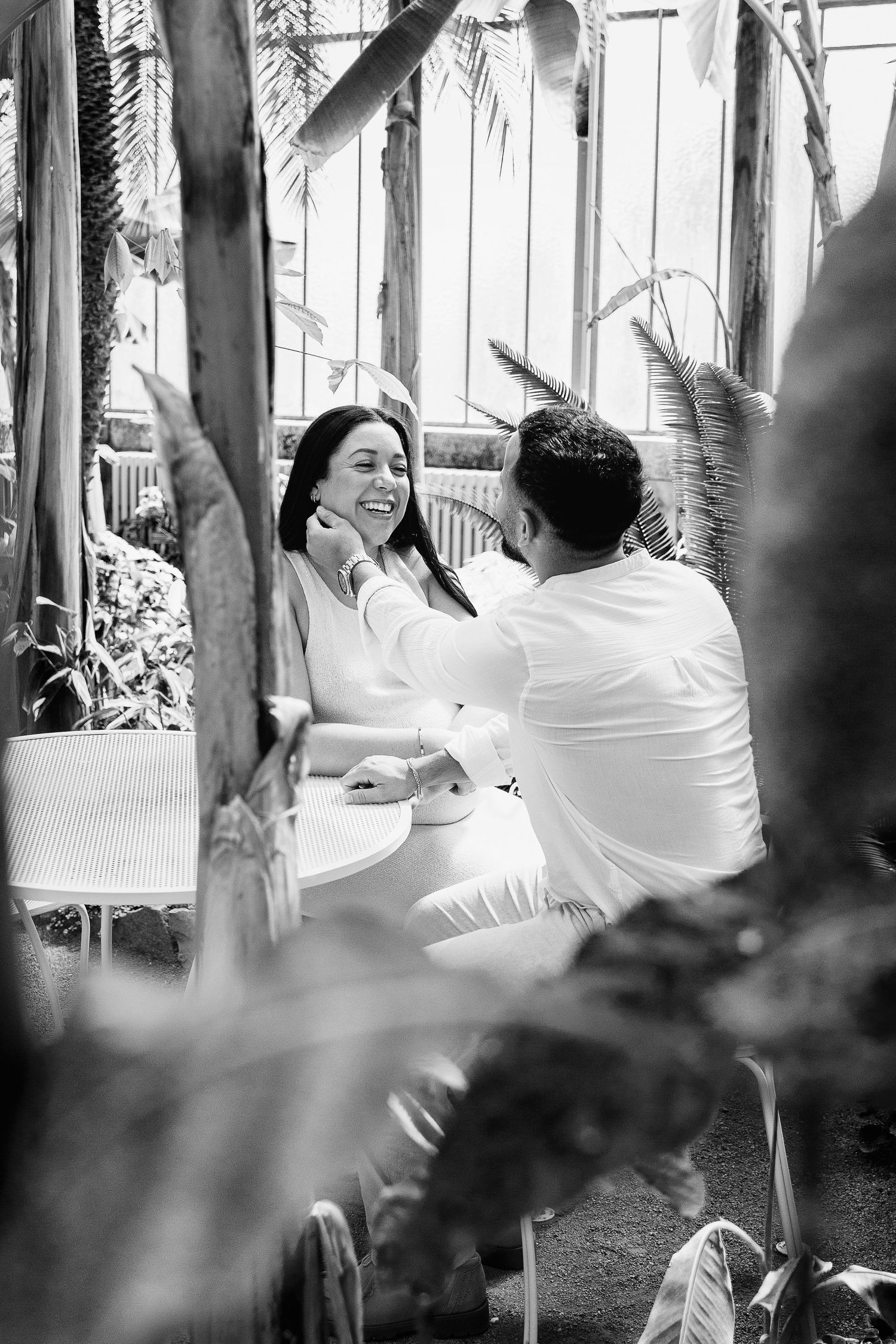 Black and white photo of a smiling couple sharing a tender moment at a table.