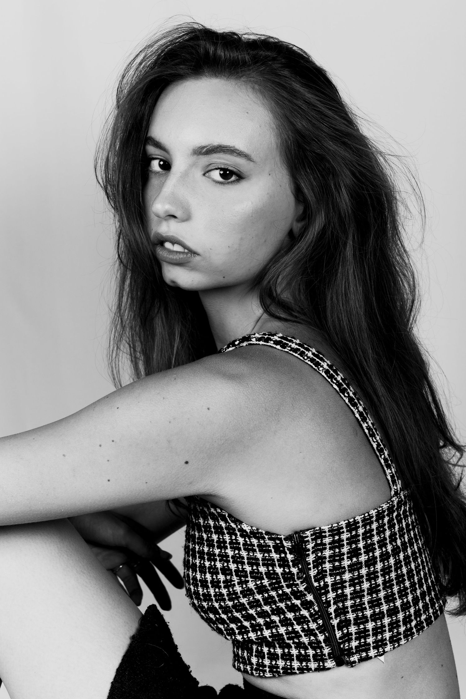 Black and white portrait of young brunette woman in checkered crop top with a captivating sideways glance.