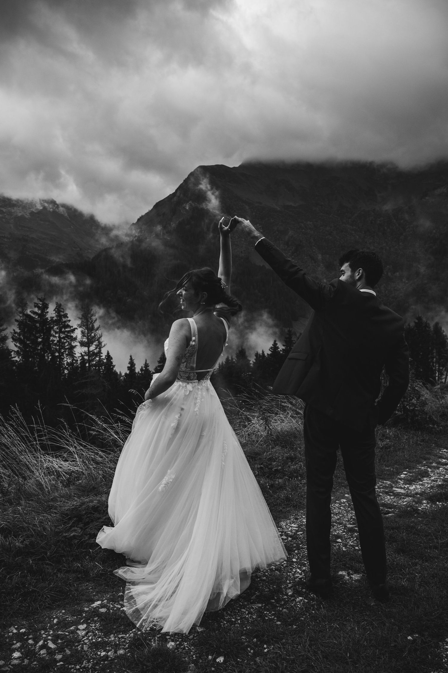Black and white photo of groom spinning bride on a misty mountain landscape.