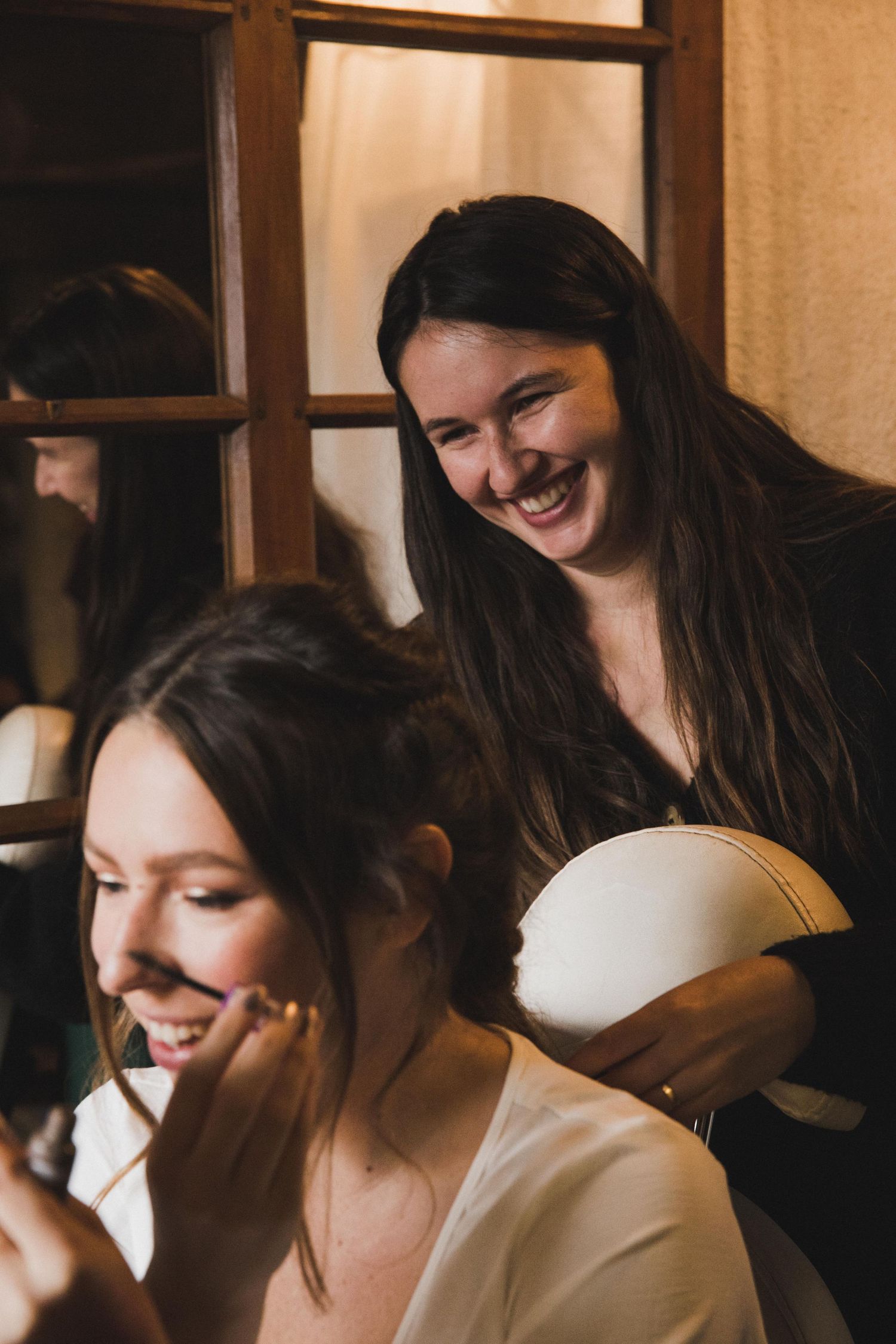 Smiling makeup artist working on brides hair and makeup before wedding ceremony.