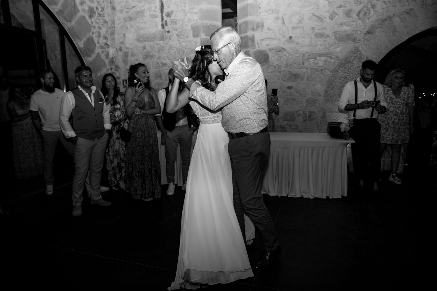 Bride and groom share their first dance at wedding reception in stone venue with guests watching.