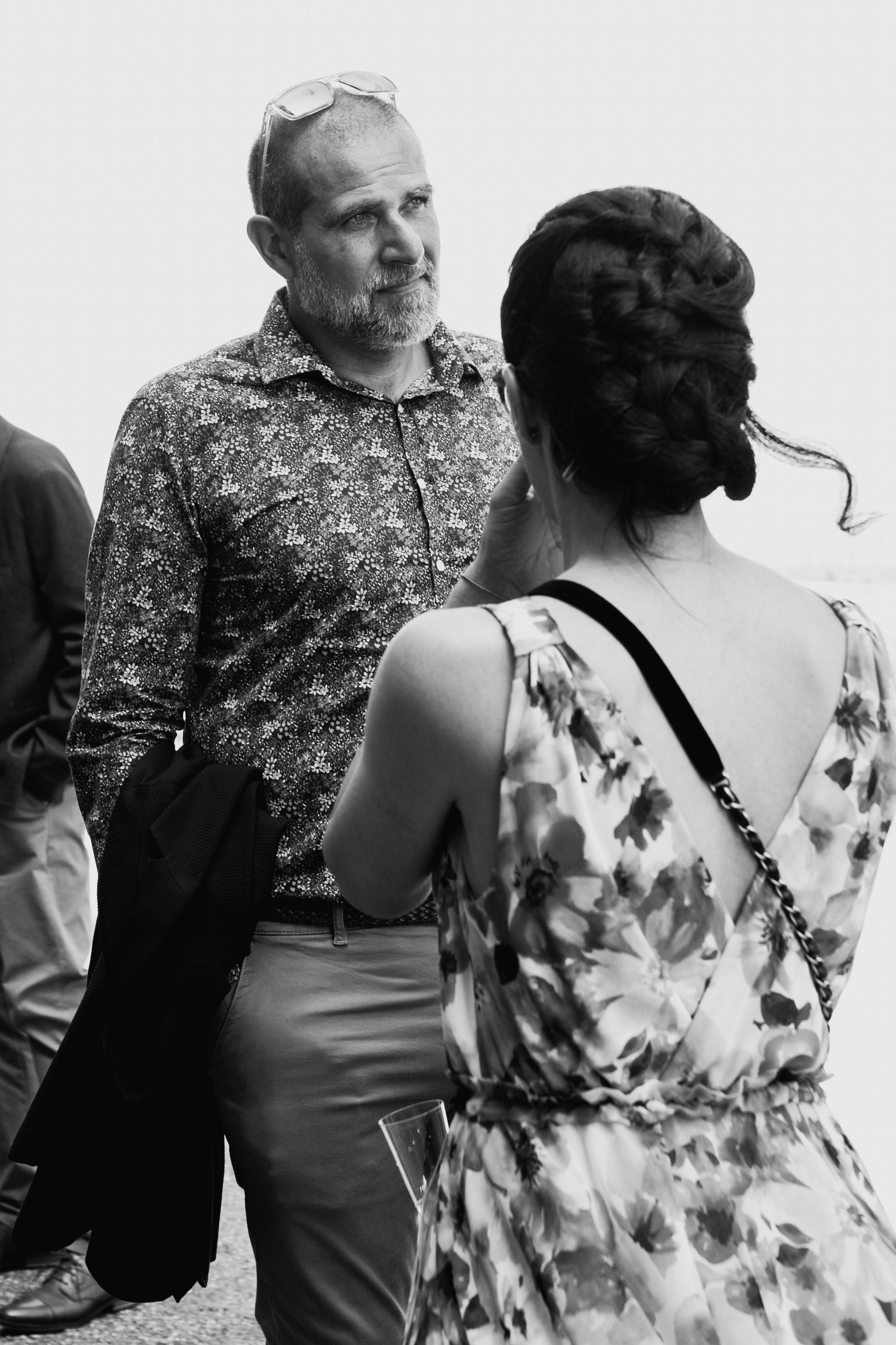 Black and white candid photo of wedding guests conversing outdoors during a celebration.