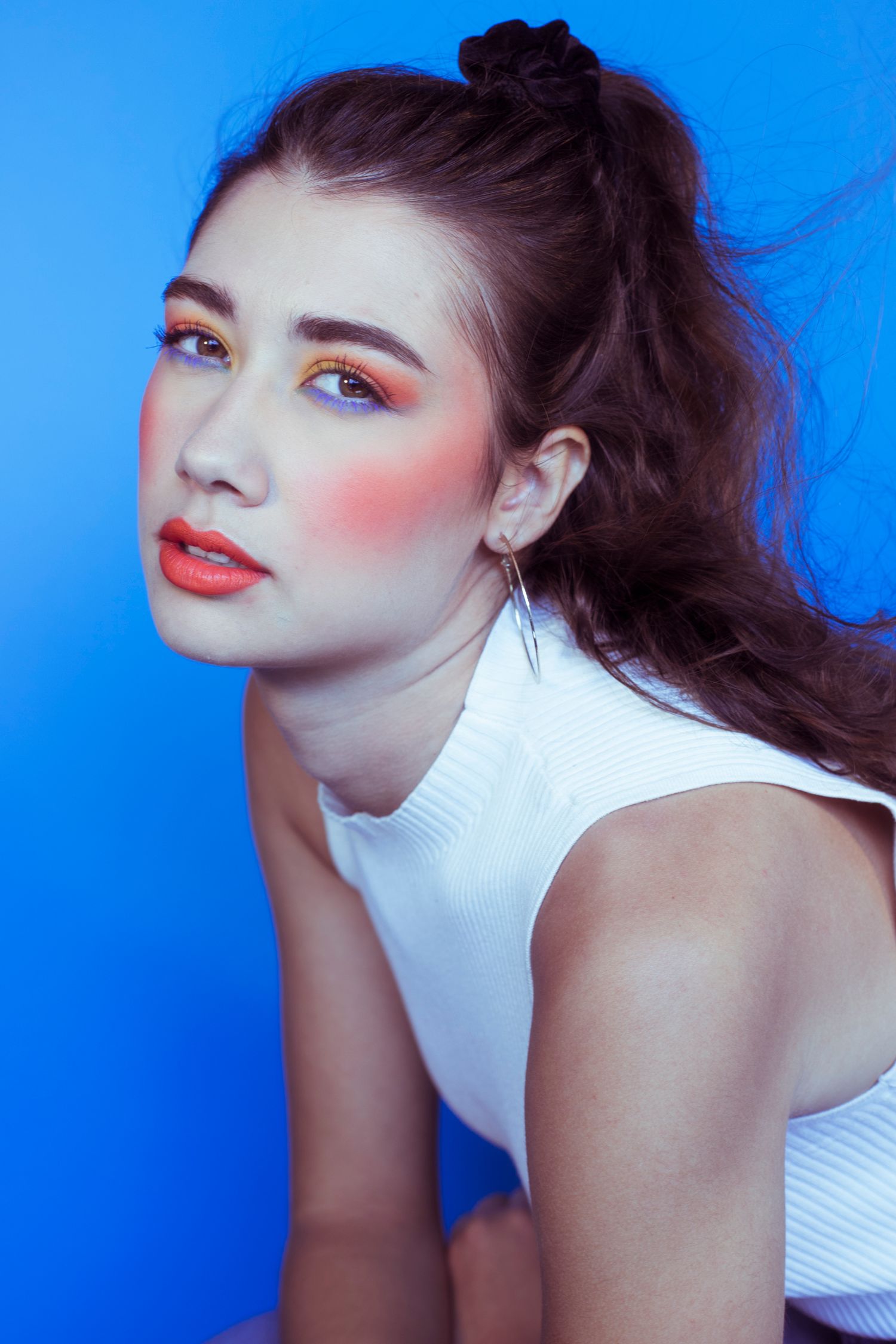 Young woman with bold orange eye makeup posing on blue background.