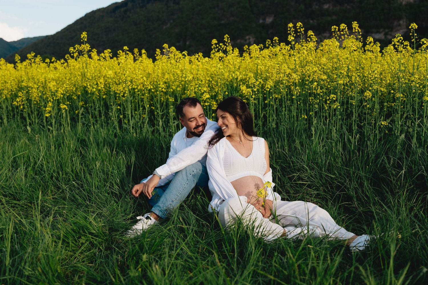 Happy couple sitting together in a vibrant yellow wildflower field during golden hour outdoors.