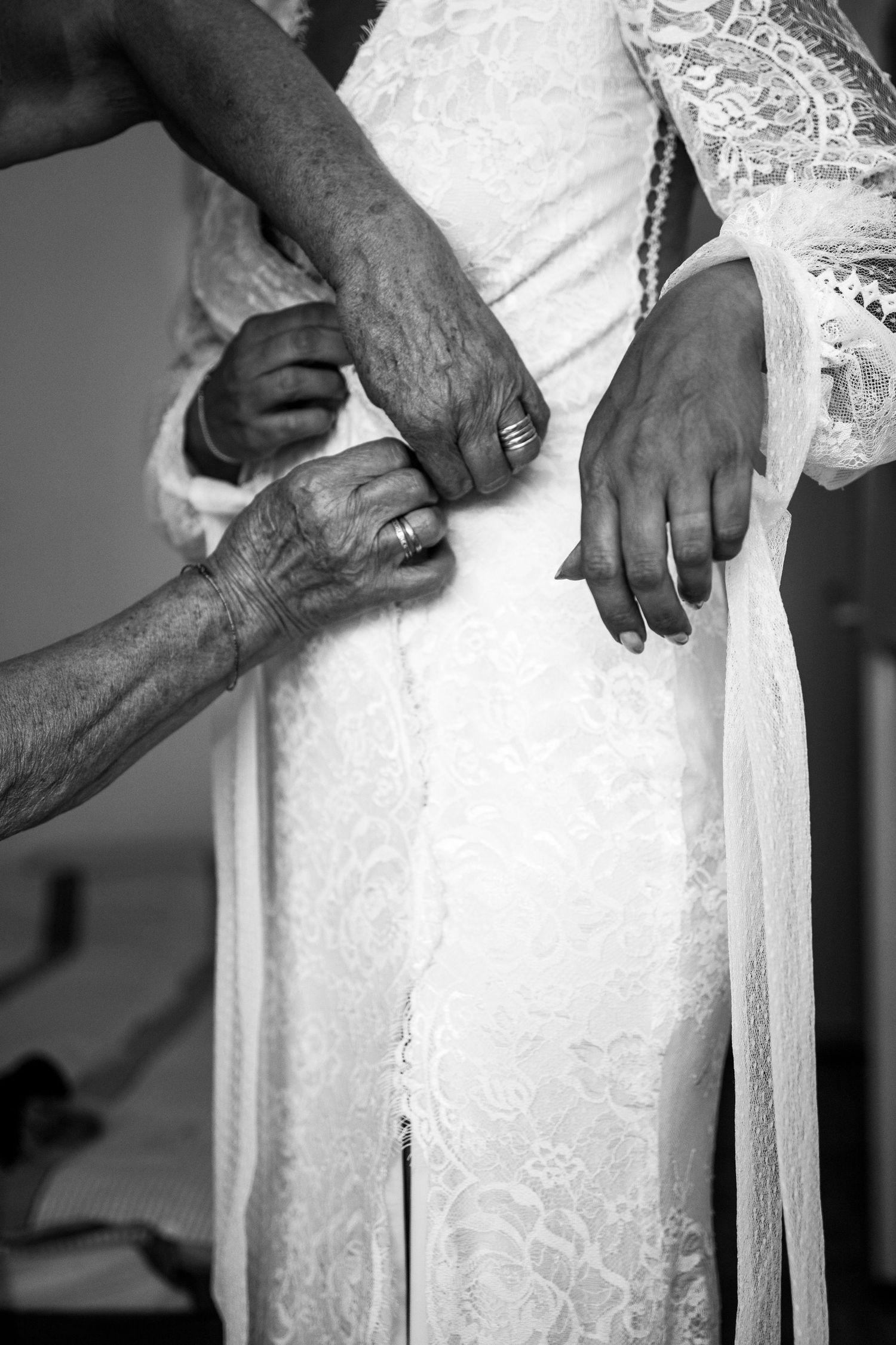 Elderly hands carefully fastening buttons on a white lace wedding dress in black and white.