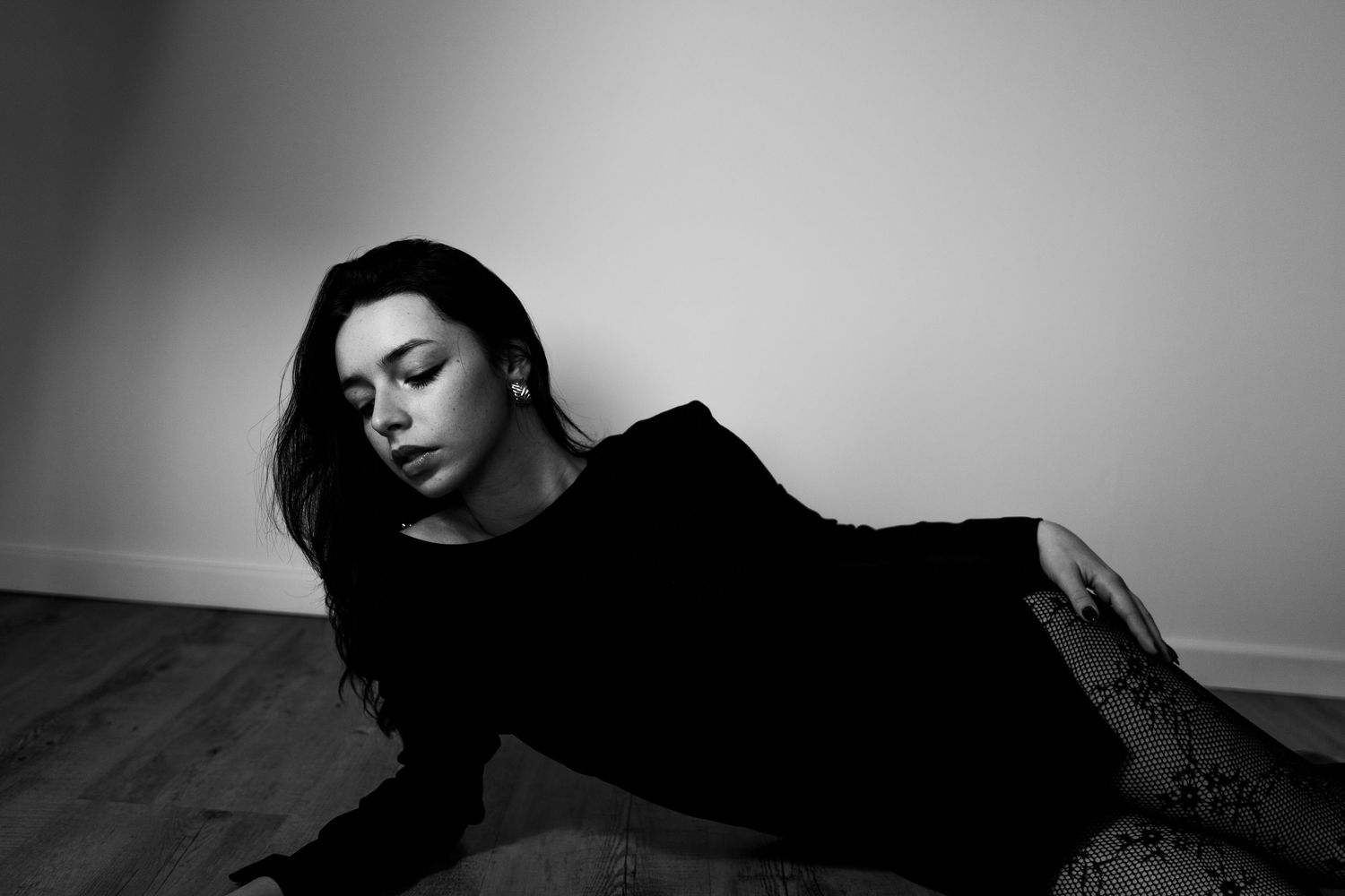 Black and white photo of woman in black dress reclining gracefully on floor.