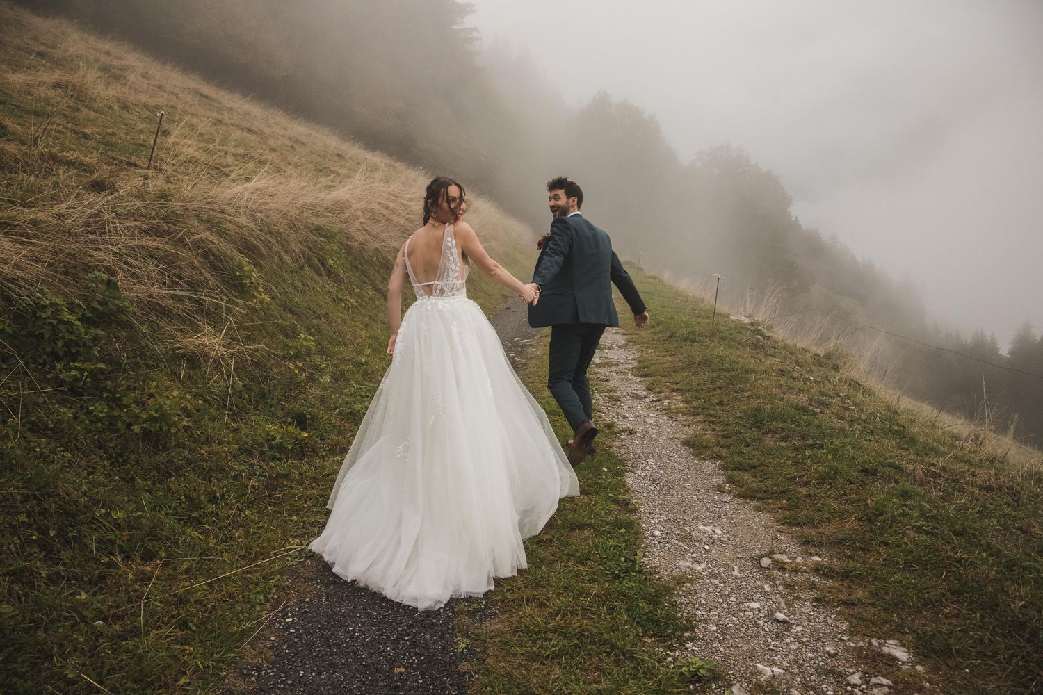 Bride and groom walking hand in hand on a foggy mountain trail on their wedding day.