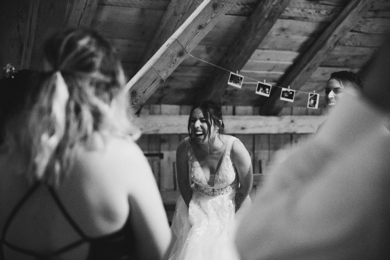 Black and white photo of bride laughing with guests in rustic barn venue.