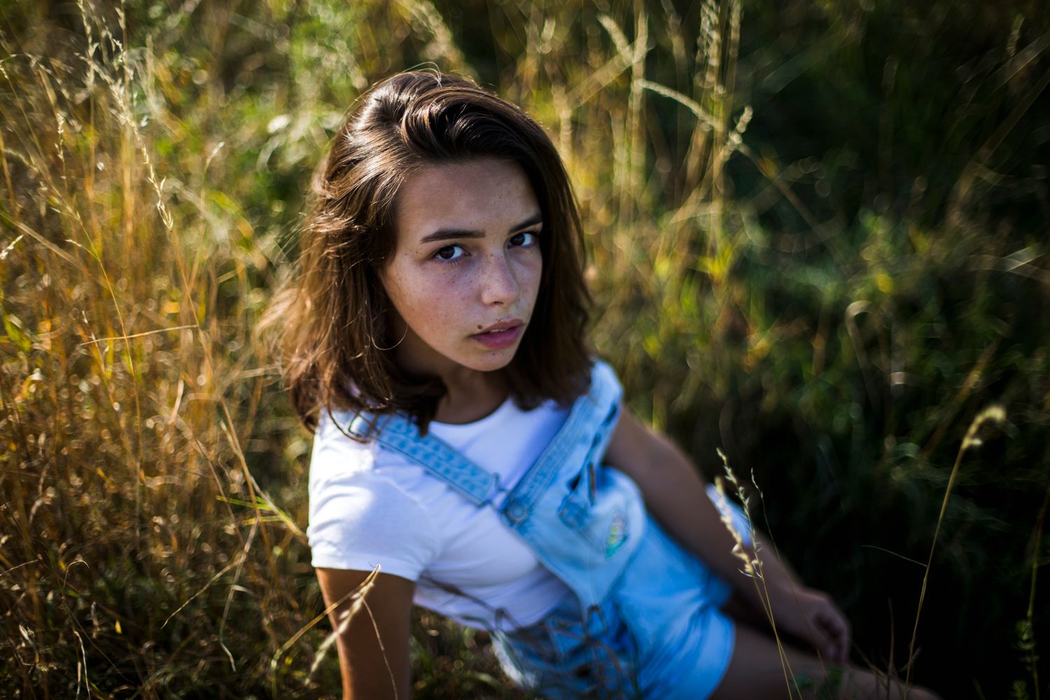 Young woman with brown hair sitting in golden sunlit grass field in outdoor portrait photography.