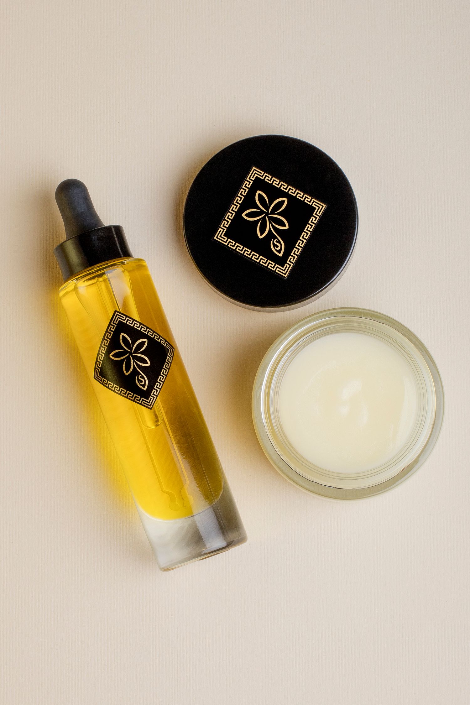 Flat lay of golden facial oil dropper bottle beside open cream jar with black luxury lid.