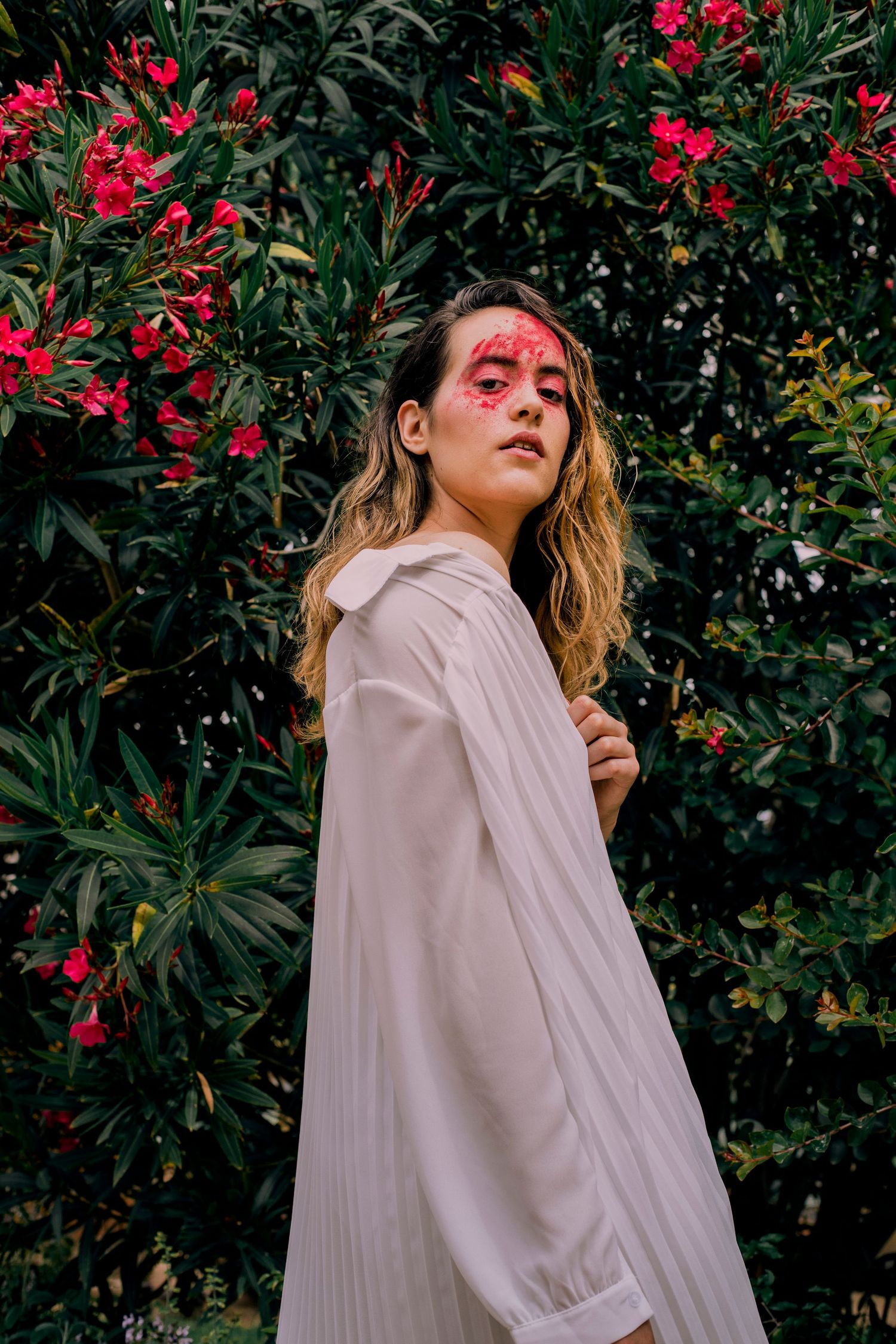 Woman with red floral face paint posing by blooming pink flowers.