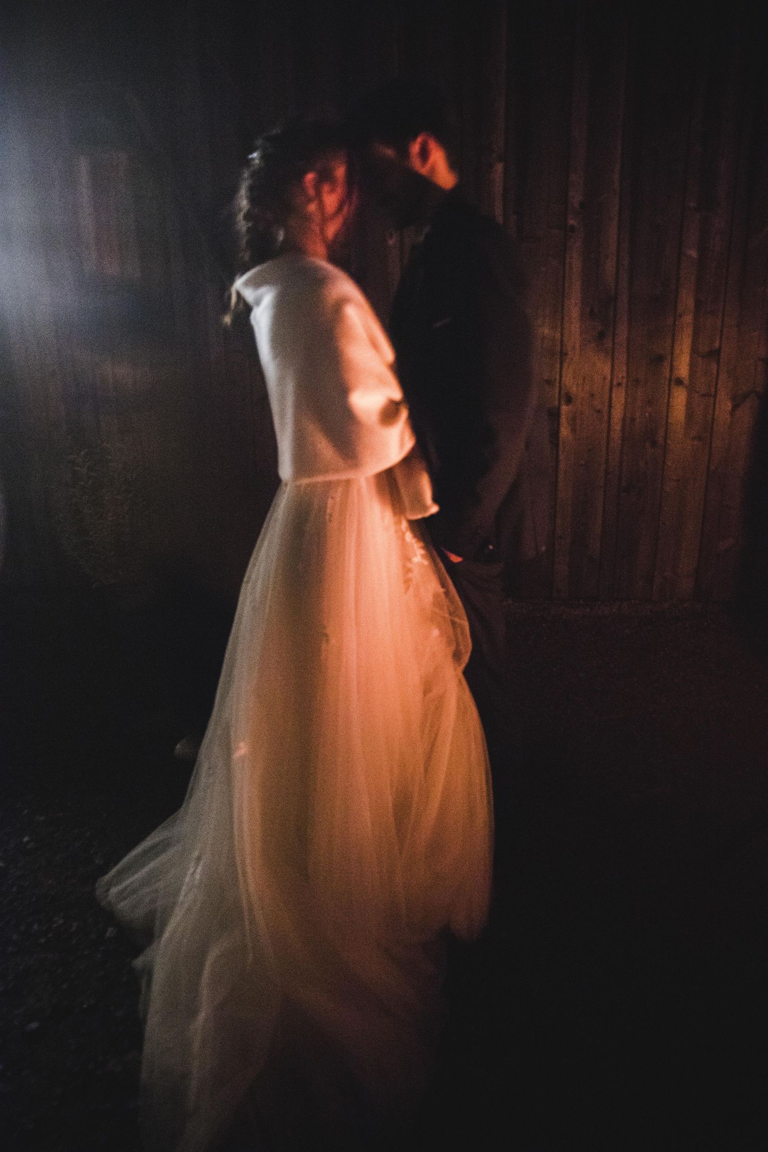 Bride and groom sharing romantic moment in dramatic light against wooden barn door.