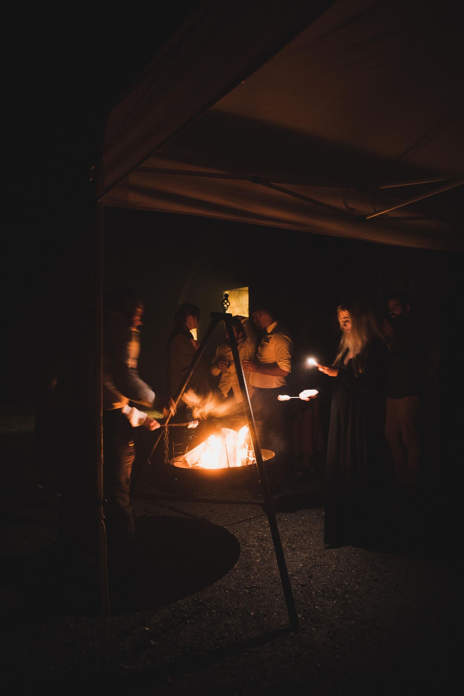 Wedding guests gathered around glowing fire pit at night outdoor celebration.
