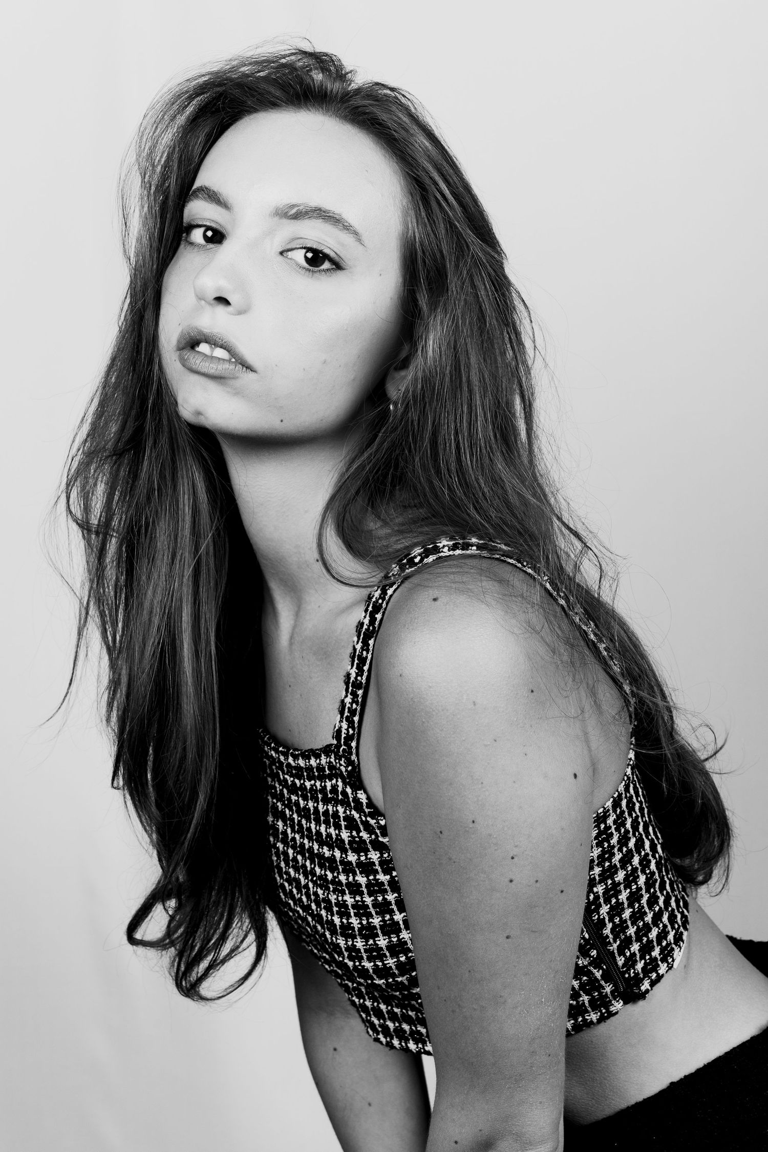Black and white side portrait of young woman with long dark hair in patterned crop top looking at camera.