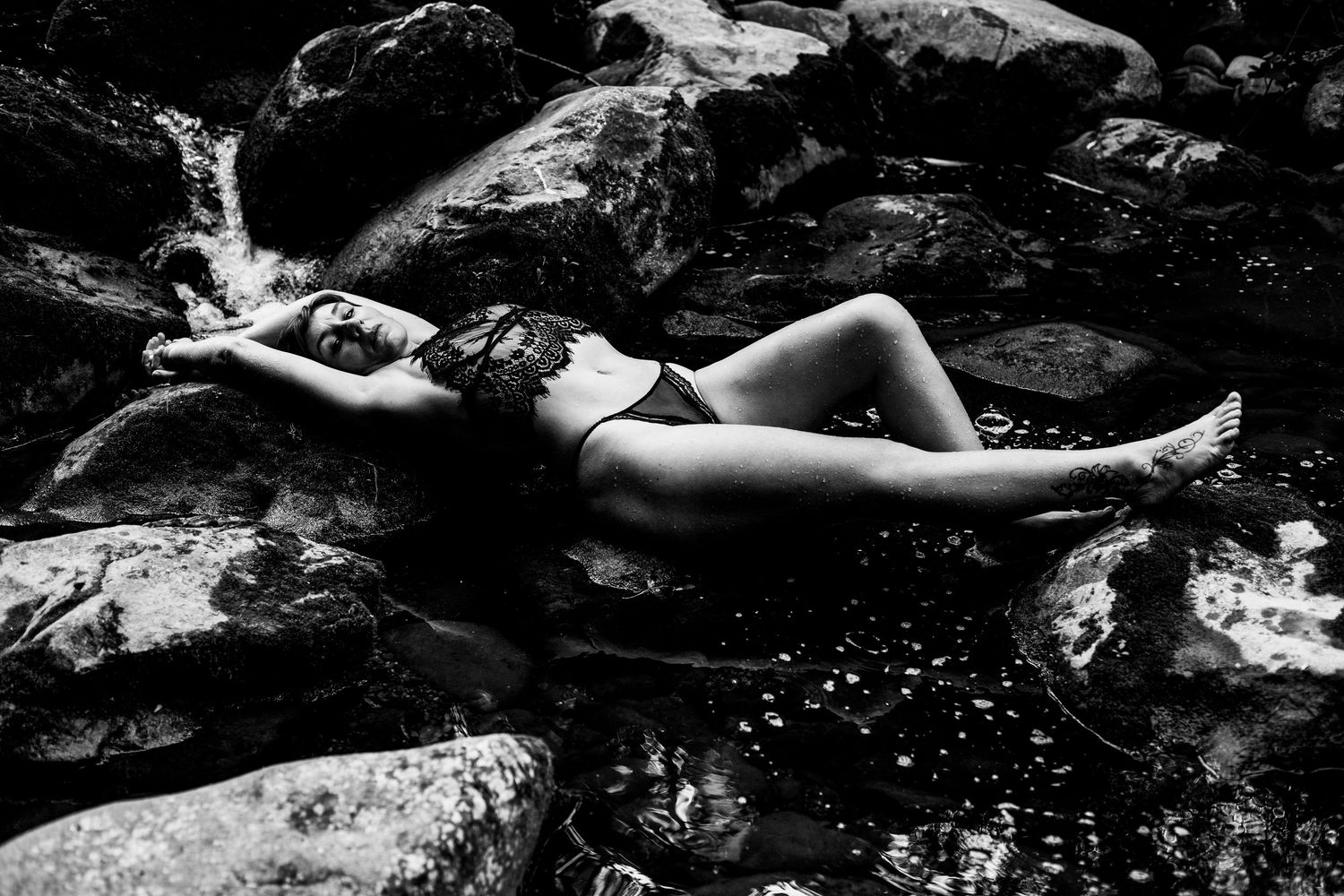 Black and white photo of a woman in a black bikini reclining on rocky terrain.