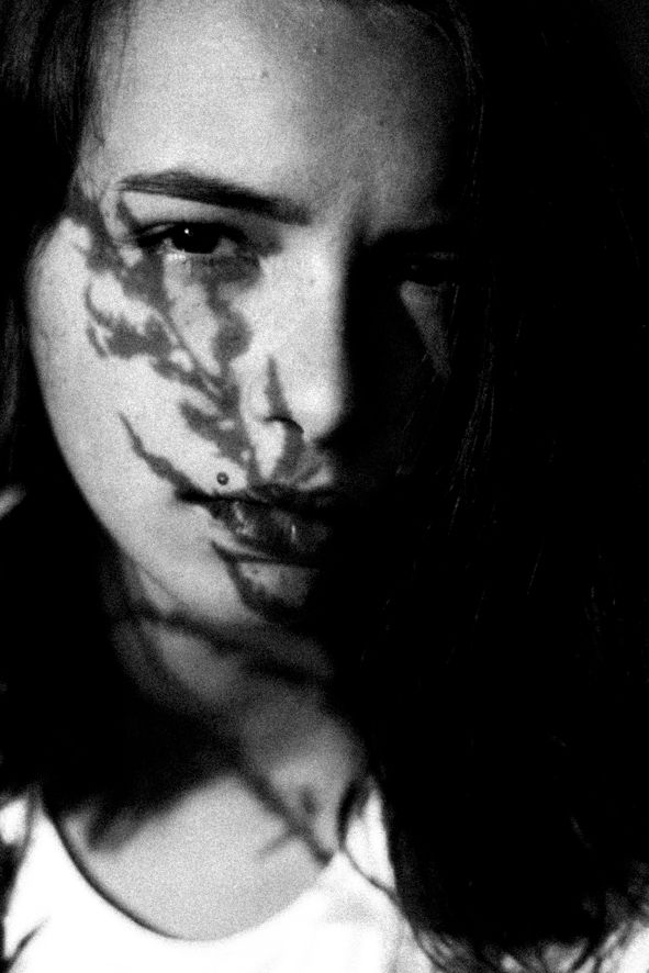 Black and white close-up portrait of a woman with leaf shadow cast across her face.