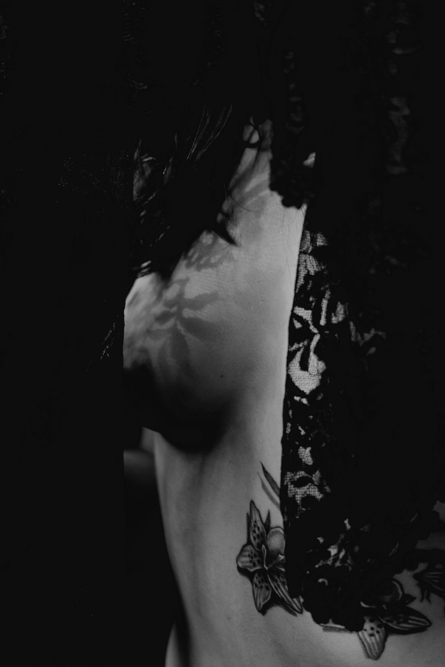 Dark black and white artistic photo of tattooed woman in black lace garment.