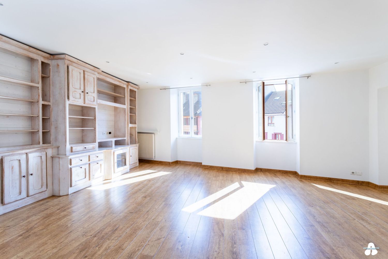 Spacious bright living room with built-in wooden shelving unit and hardwood floors.