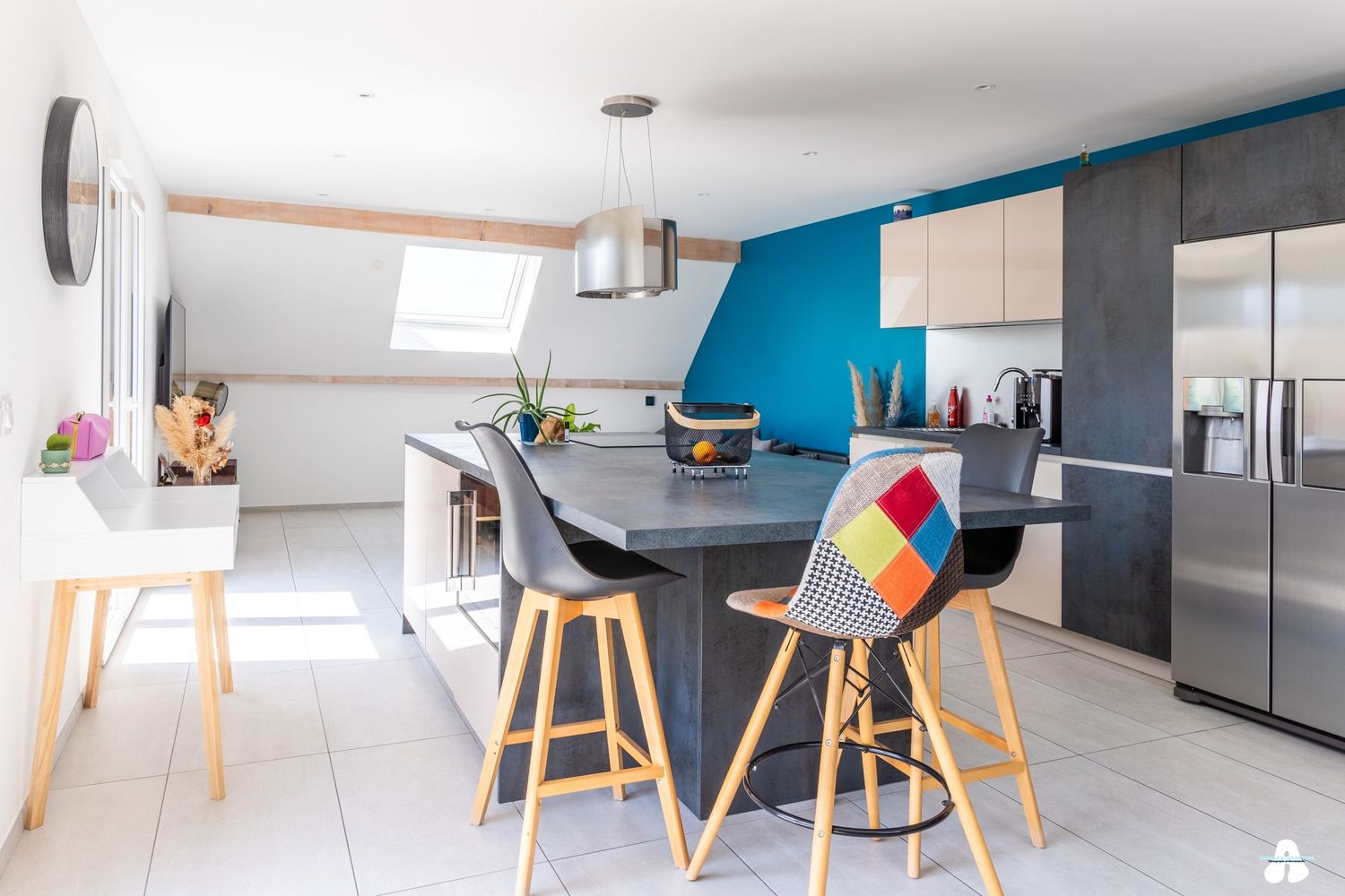 Bright open-plan kitchen featuring blue wall, gray cabinetry, multicolor chairs, and stainless steel fridge.