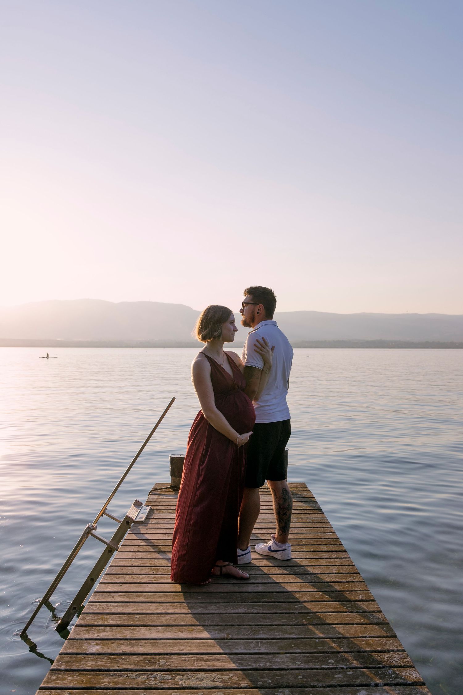 Couple embracing on a wooden dock at sunset over a calm lake with mountains in the background.