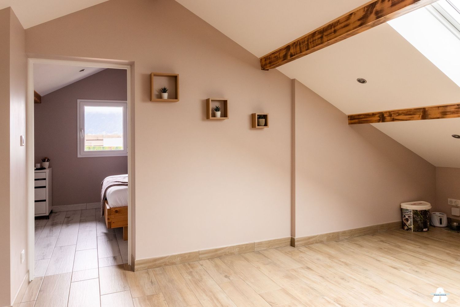 Light attic landing with exposed wooden beams, light wood floors and view into bedroom.