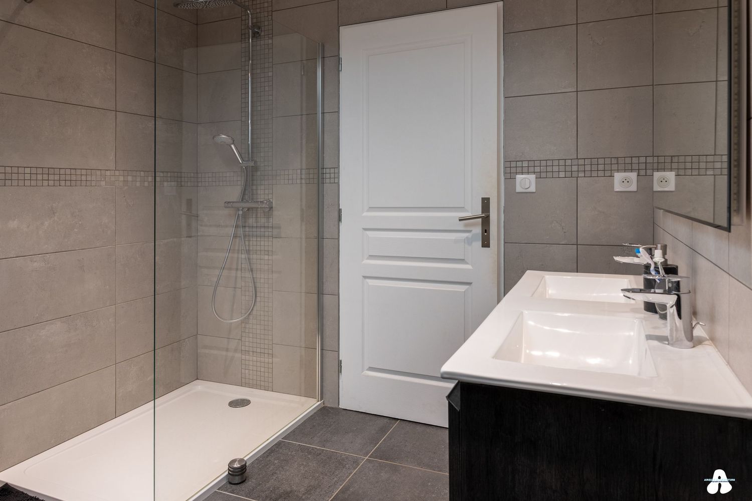 Modern bathroom with large walk-in shower, double white sink vanity and grey tile walls.