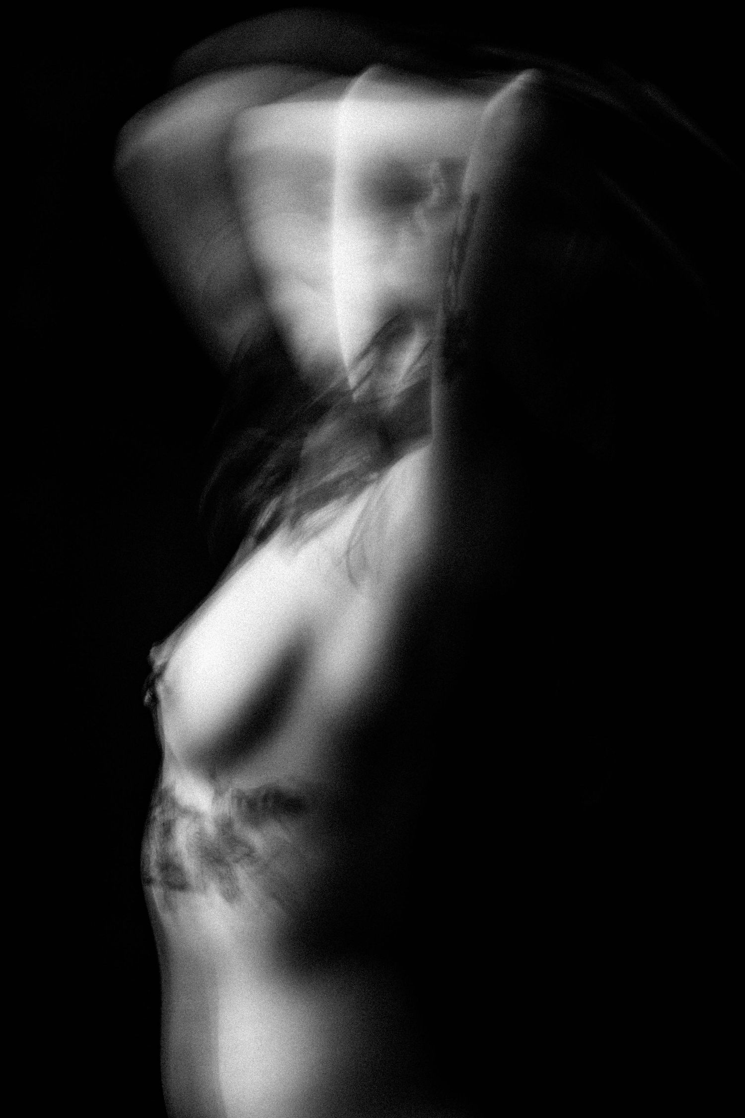 Blurred black and white artistic nude photo capturing motion and form against dark background.