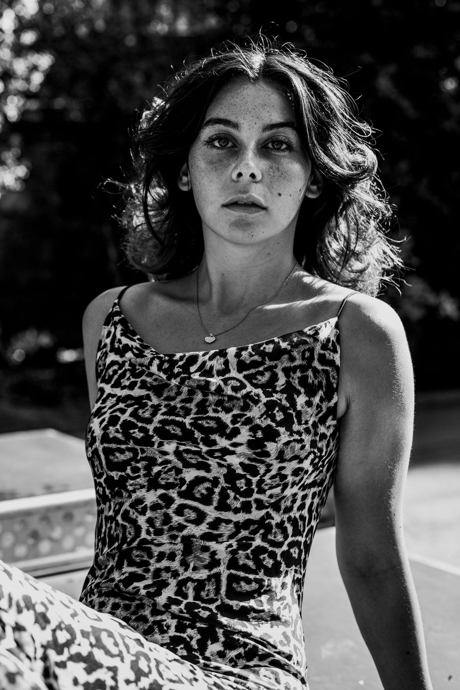 Black and white portrait of a young woman in a leopard print dress sitting outdoors in natural light.