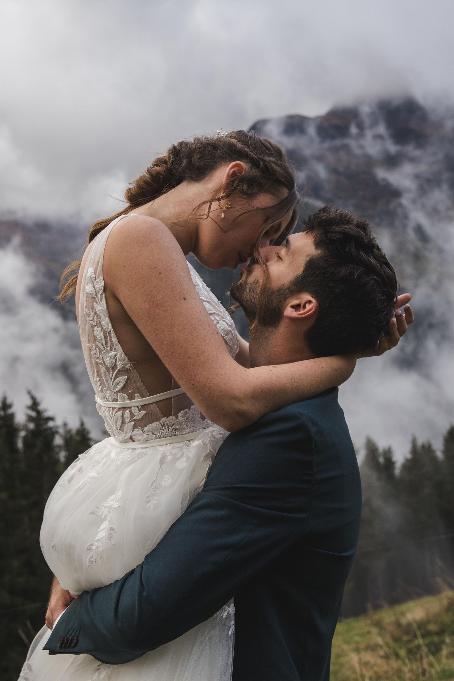 Groom lifting bride as they share a kiss with foggy mountain forest in the background.
