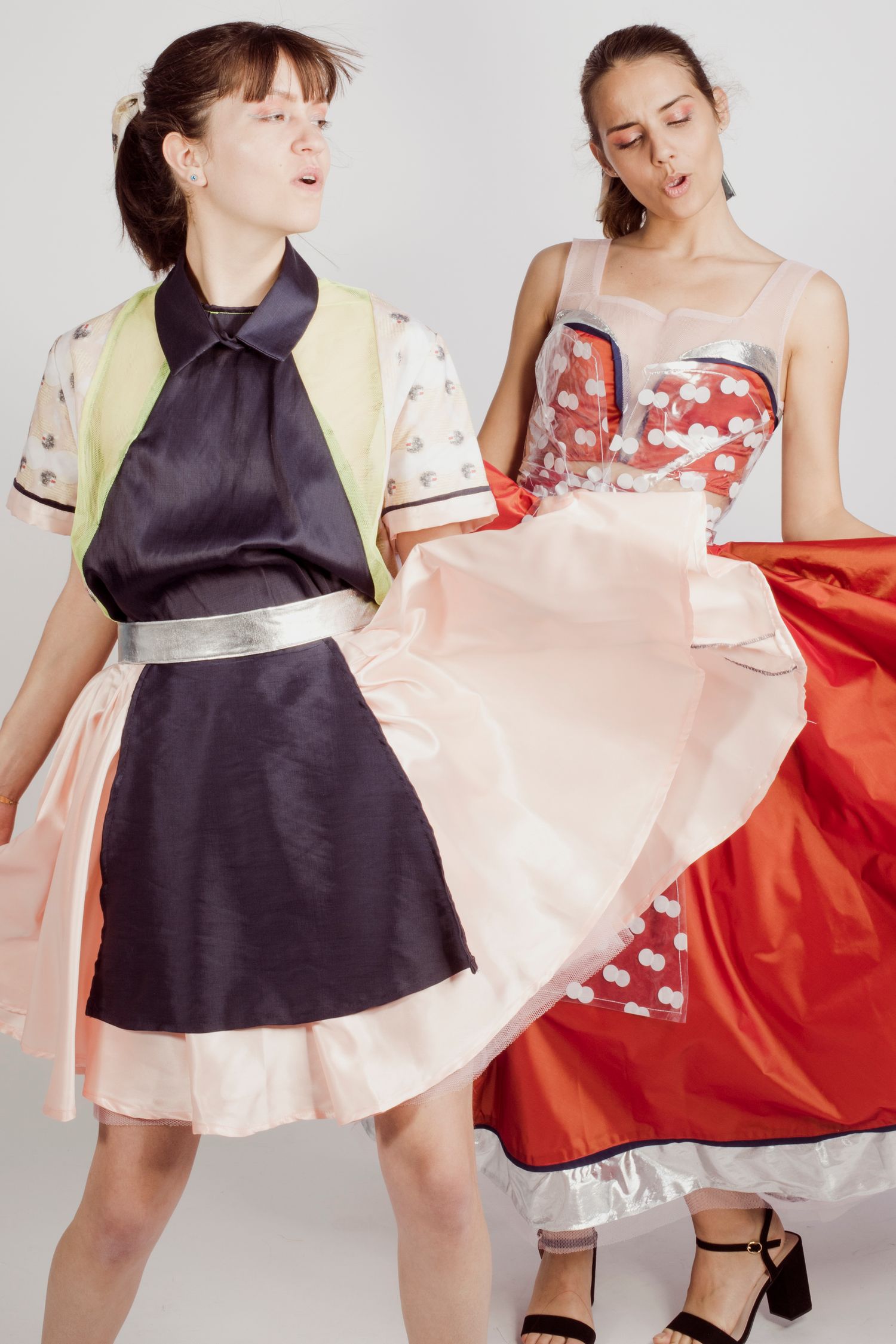 Two young women model colorful avant-garde fashion designs in a studio setting.