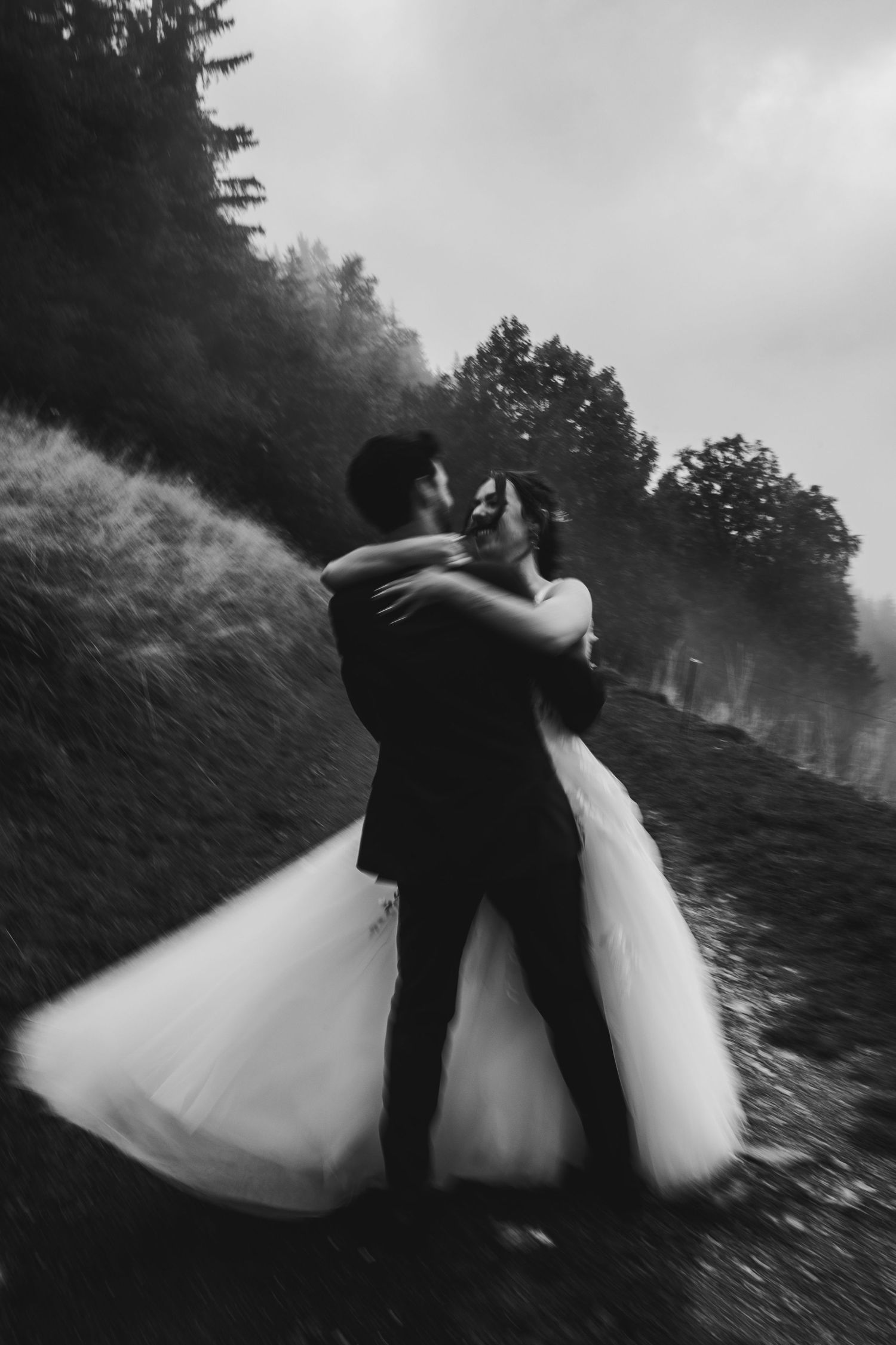 Black and white photo of bride and groom embracing on misty hillside with flowing wedding dress.