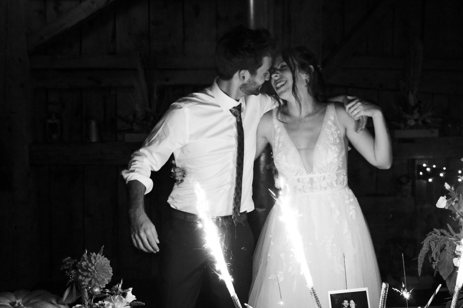 Black and white photo of joyful bride and groom celebrating with sparklers at their wedding reception.