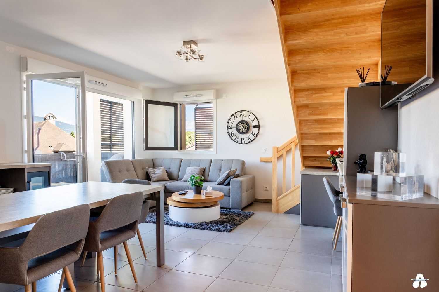 Open plan living and dining room with wooden staircase, large windows, and modern furnishings.