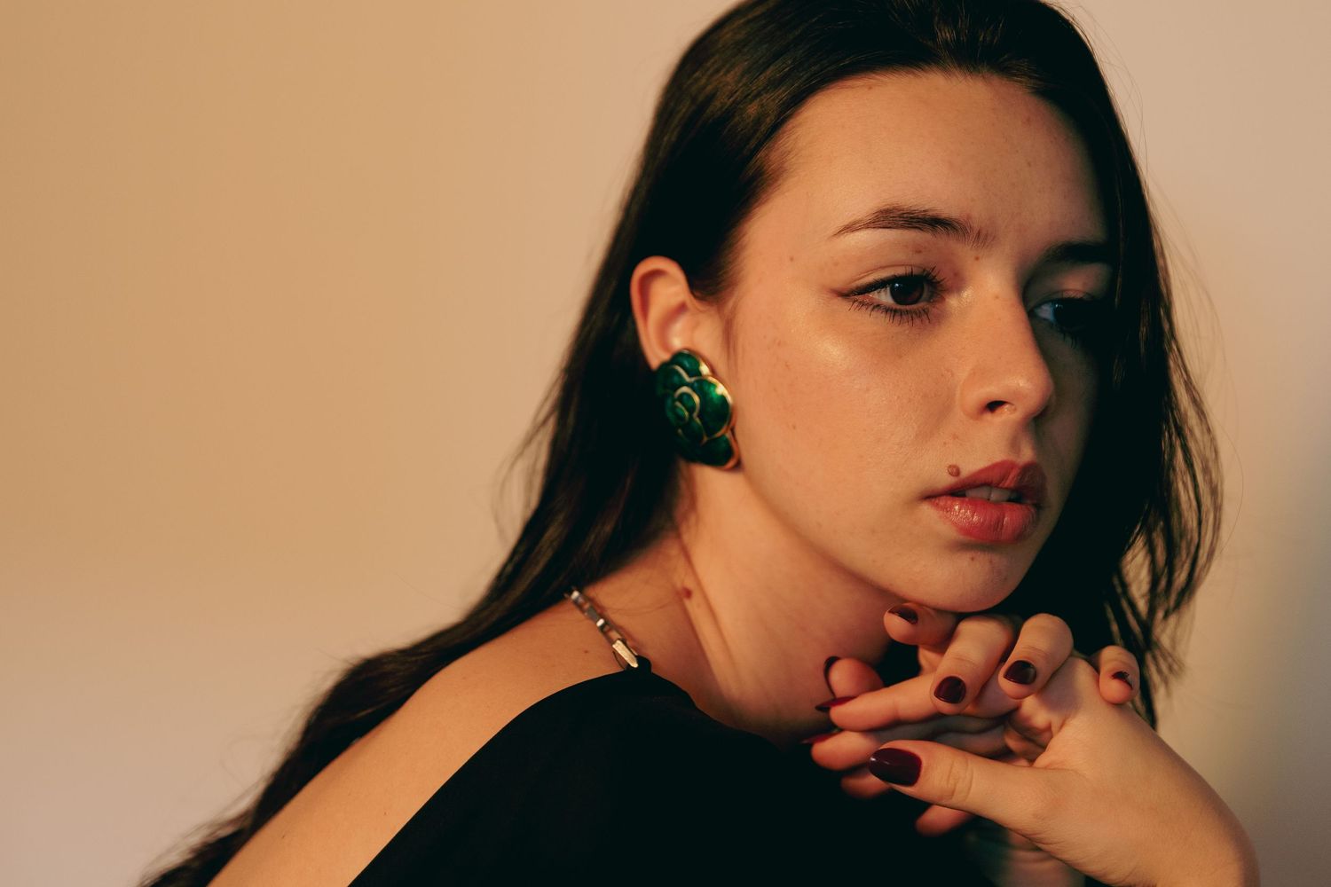 Close-up portrait of woman wearing large green earrings and black top with gold necklace.