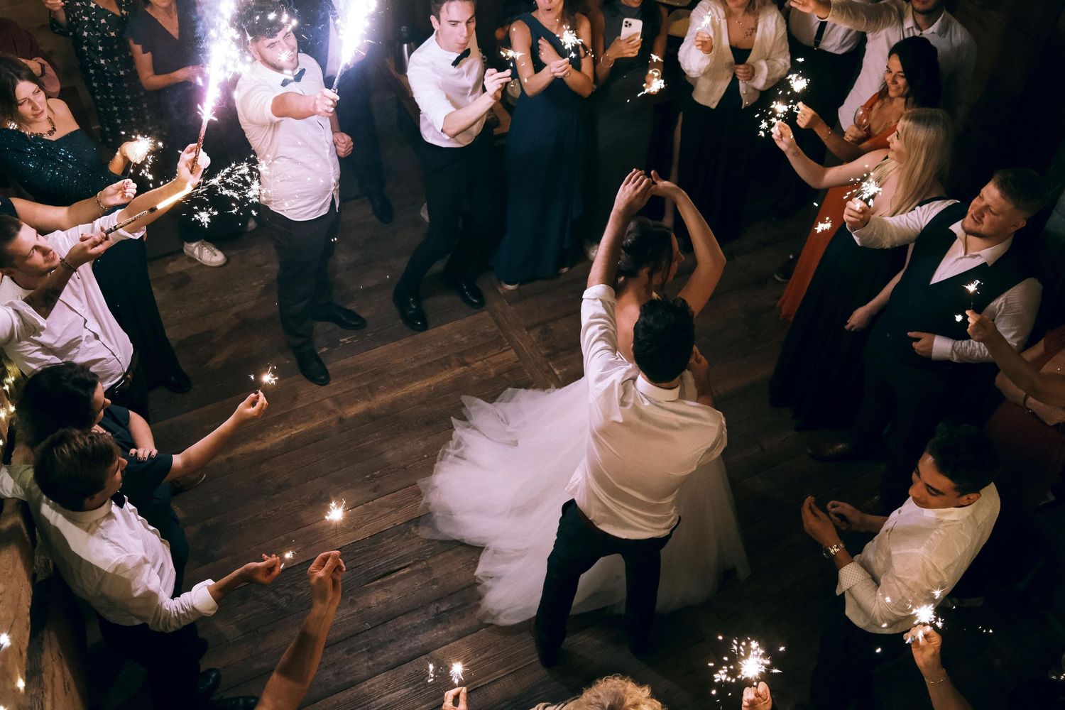 Bride and groom dancing surrounded by wedding guests holding sparklers in a barn venue.