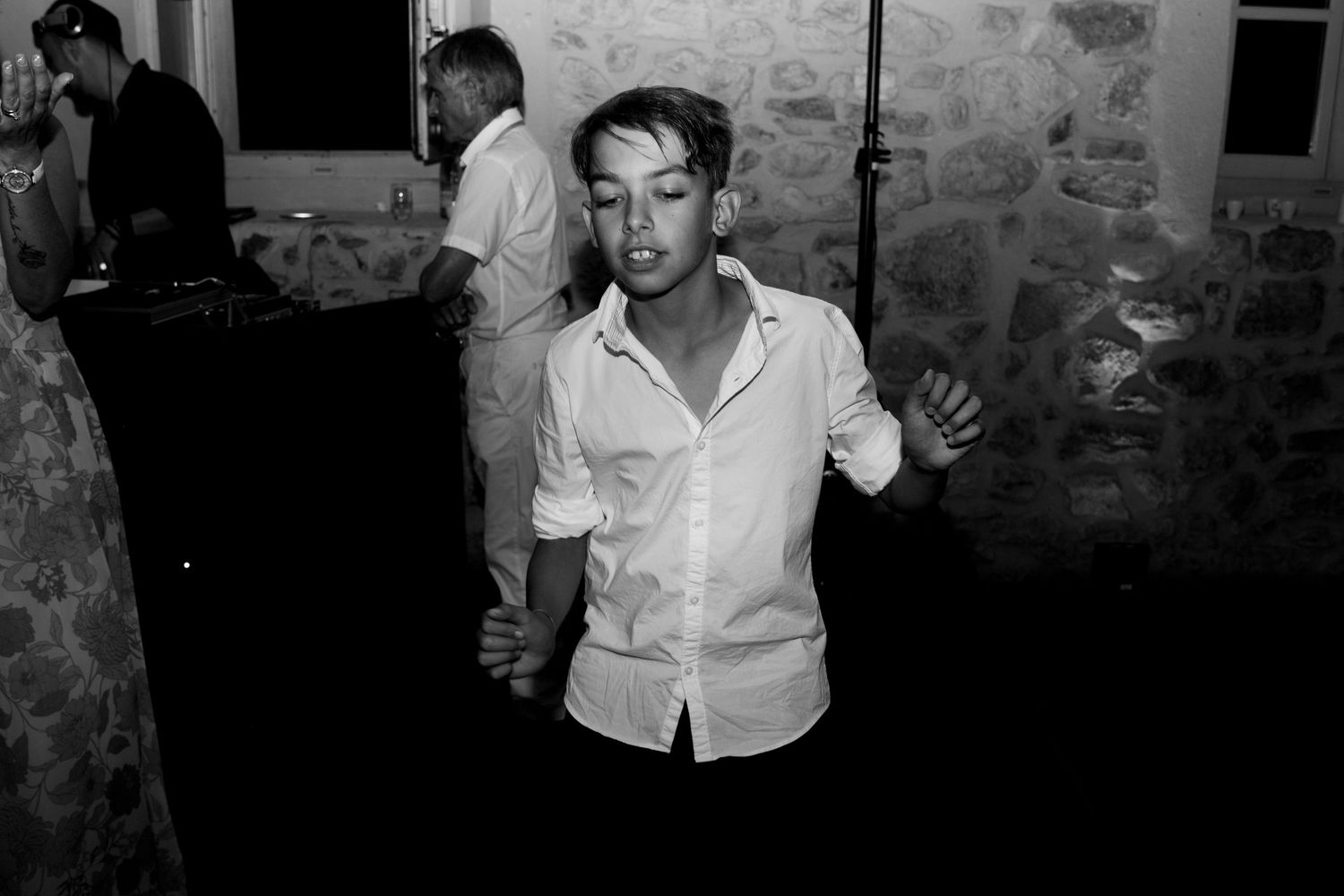 Young boy dancing energetically at wedding reception in dimly lit stone venue.