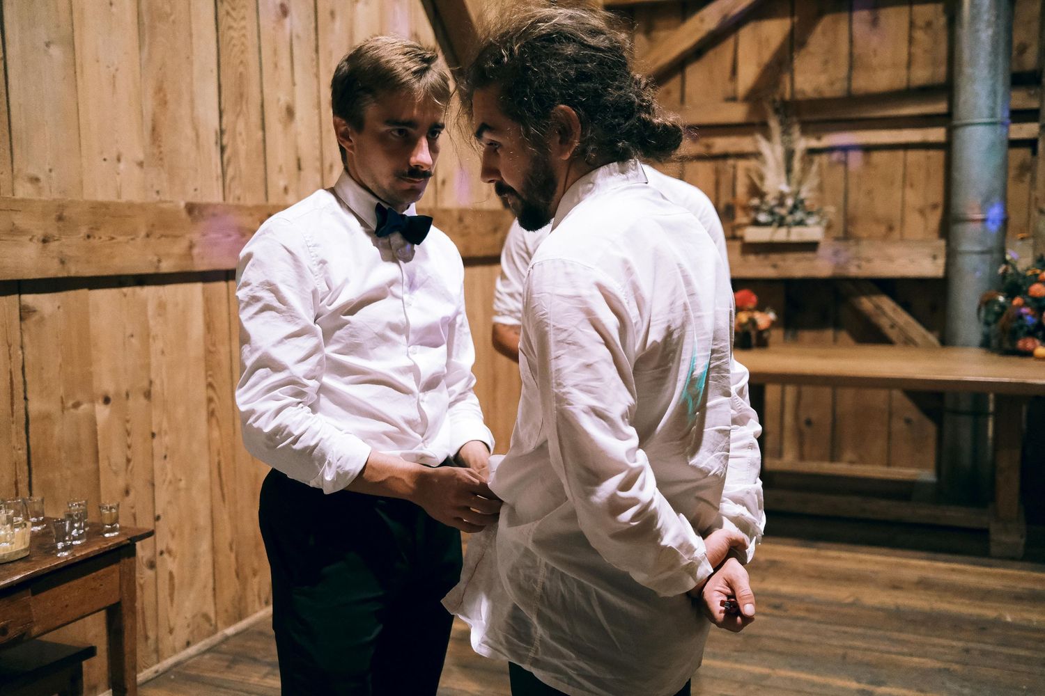 Two men in white dress shirts having an intimate conversation in a rustic barn setting.