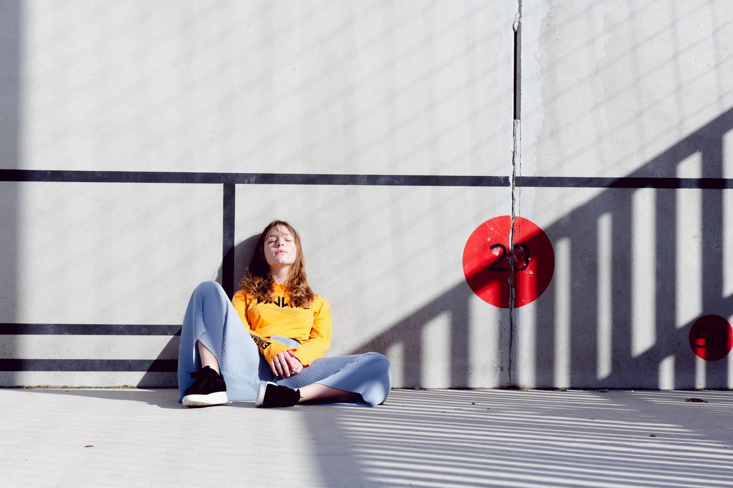 Young woman in yellow sweater and jeans sitting cross-legged on ground near red circular decorations.