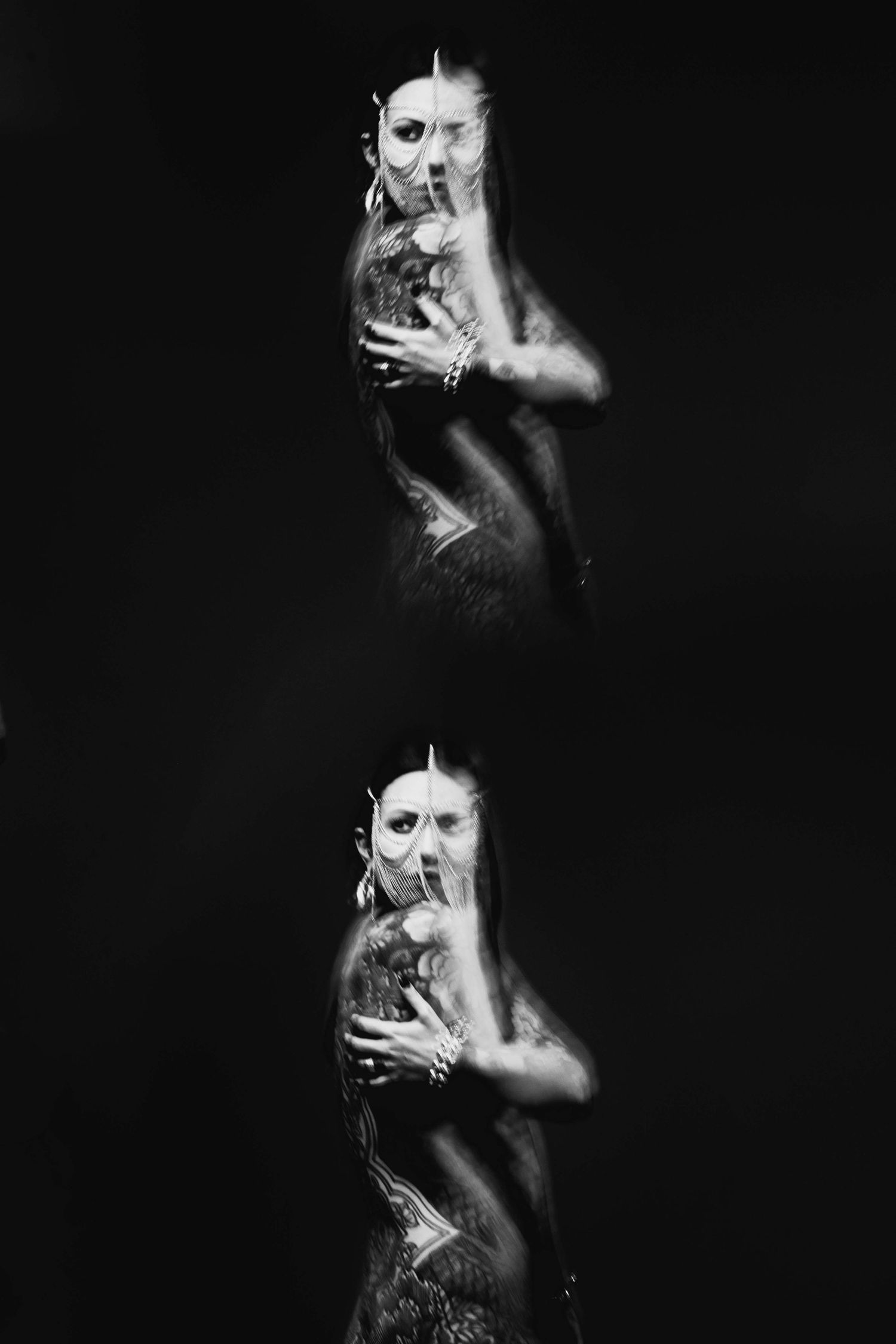 Black and white double exposure portrait of tattooed woman in dramatic dark studio setting.