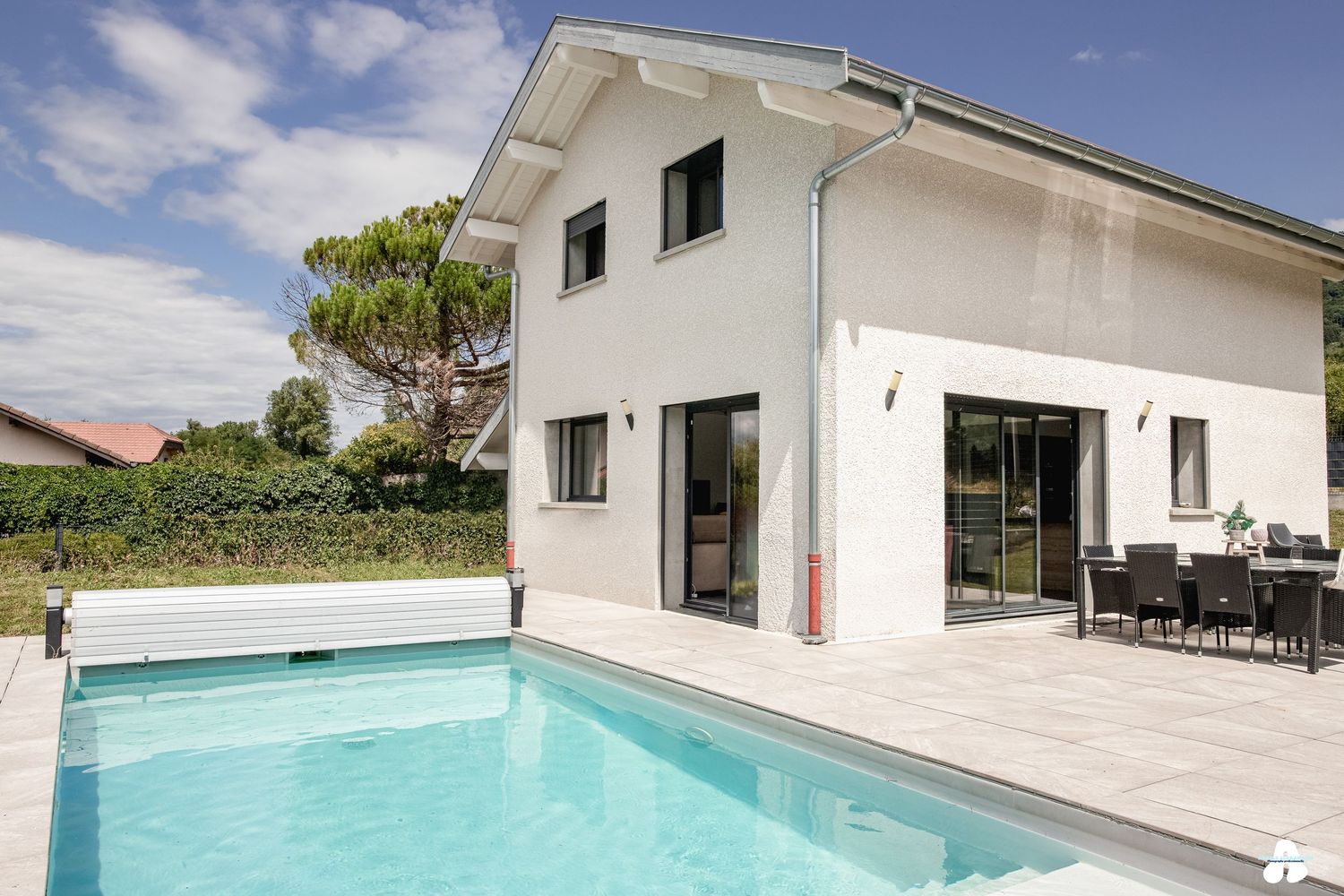 Modern white two-story villa with large swimming pool and outdoor dining area surrounded by greenery.